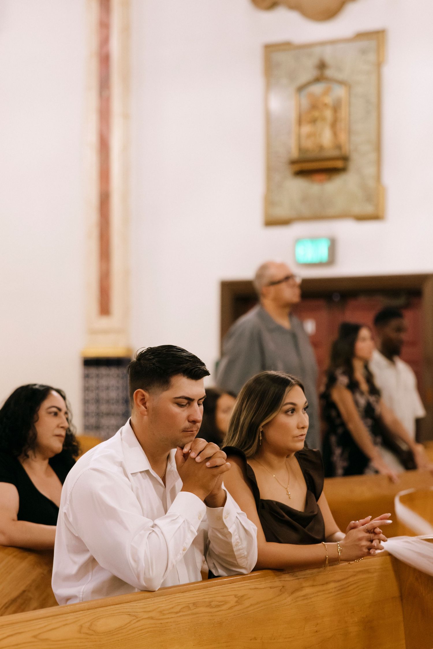 People praying while seated in wooden church pews during a religious service.