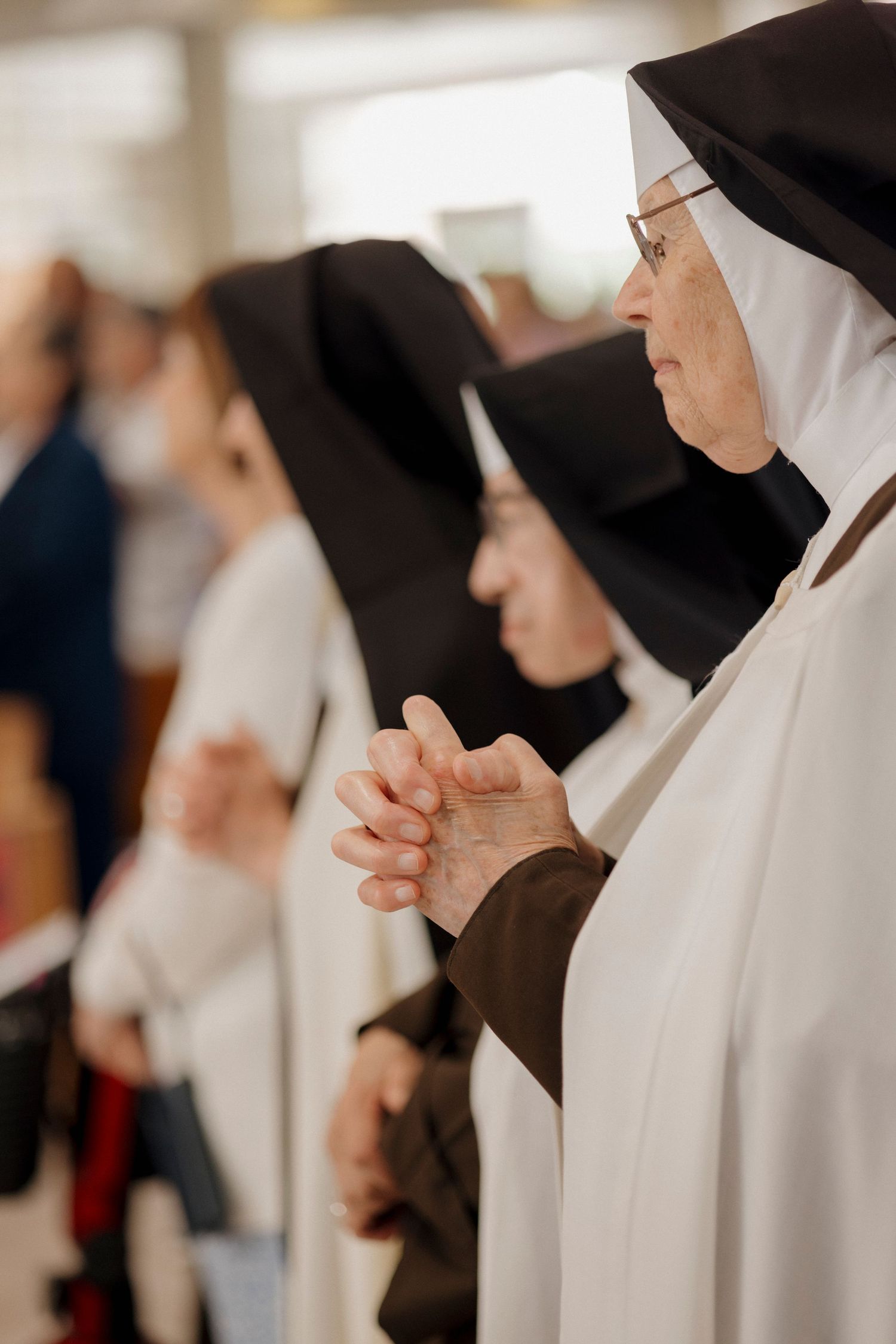 Nuns in traditional black and white habits stand in prayer during a religious service.