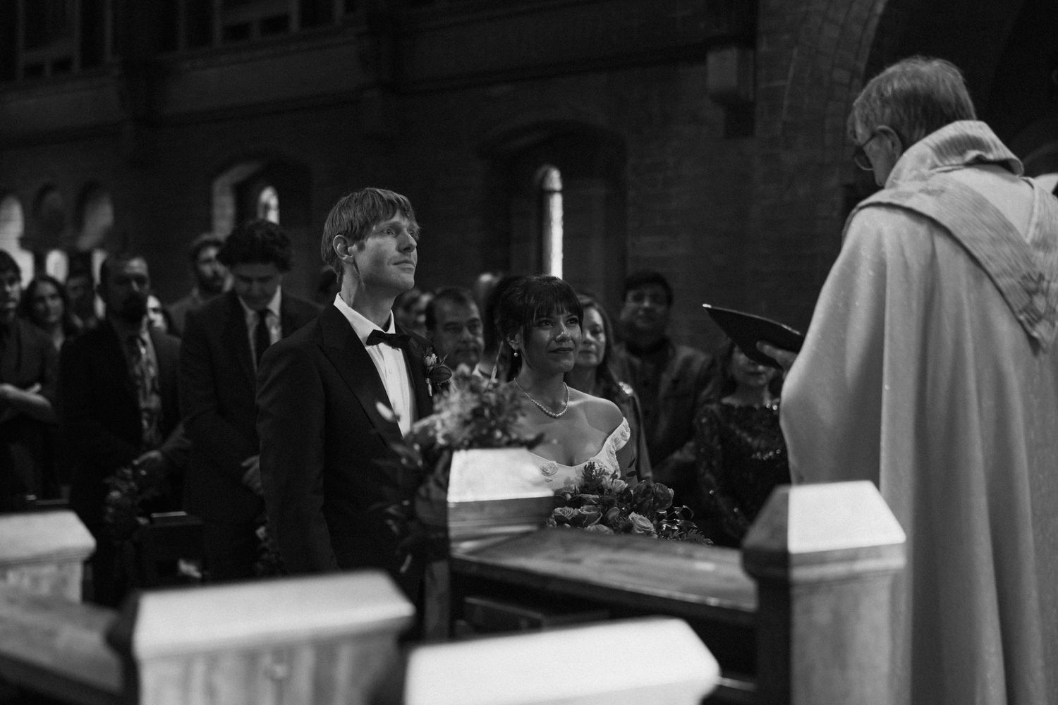 Dark interior of church sanctuary with guests seated during wedding ceremony.