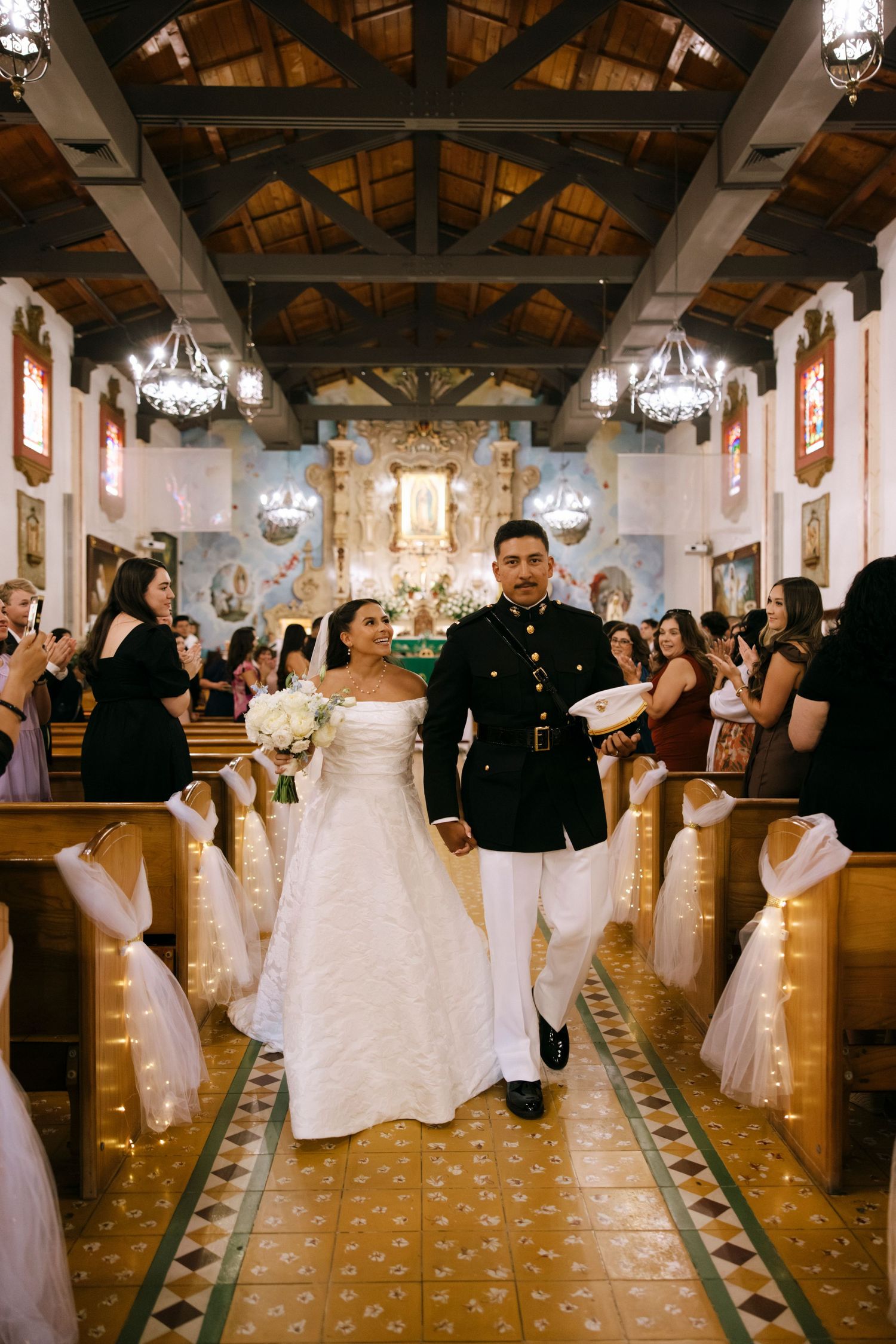 Wedding celebration in a church hall with wooden beams and chandeliers overhead.