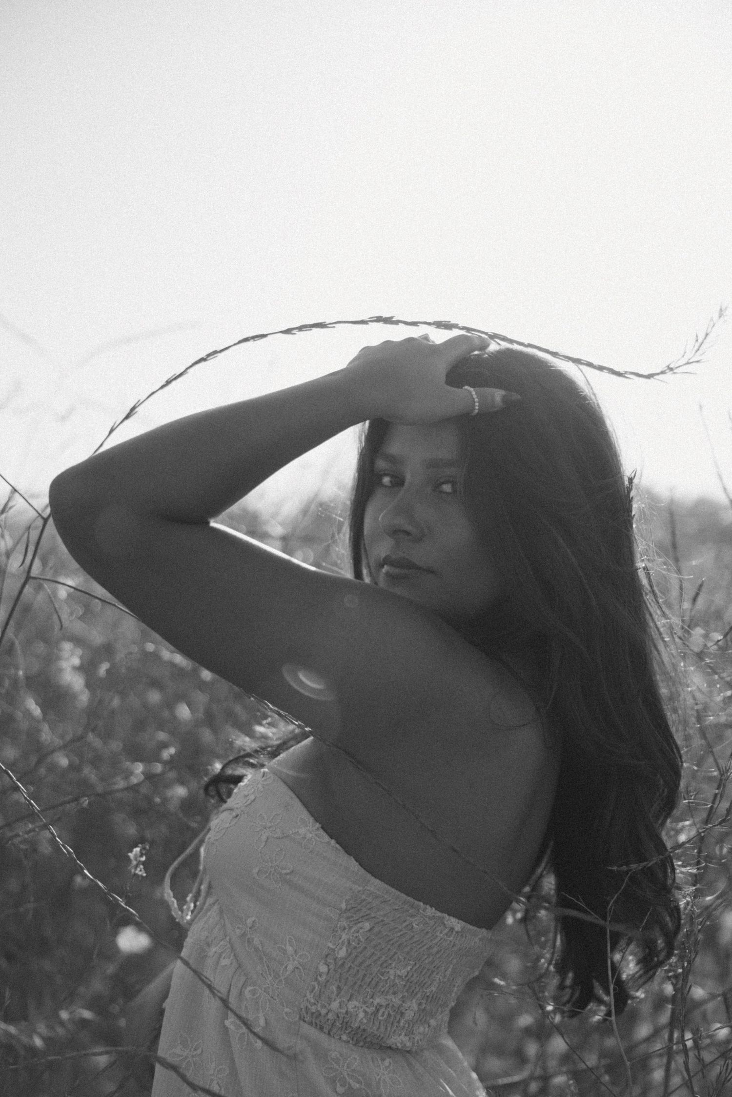 Woman in white dress poses dramatically in black and white portrait.