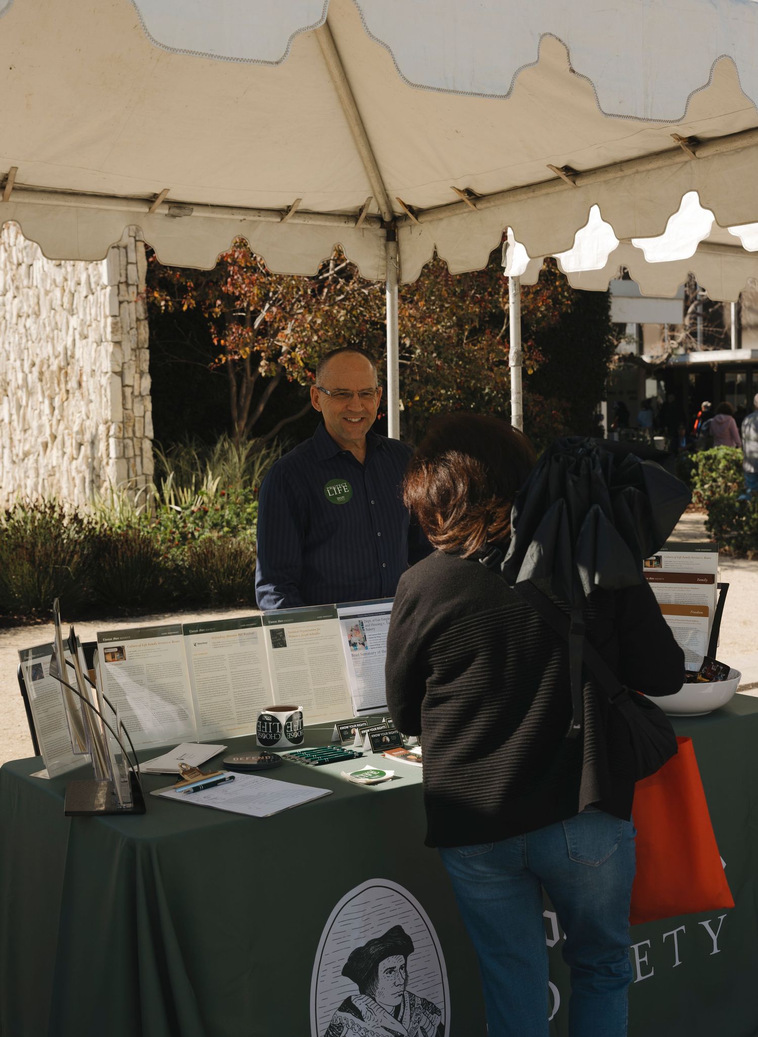 Visitors browsing information displays under a white event tent.