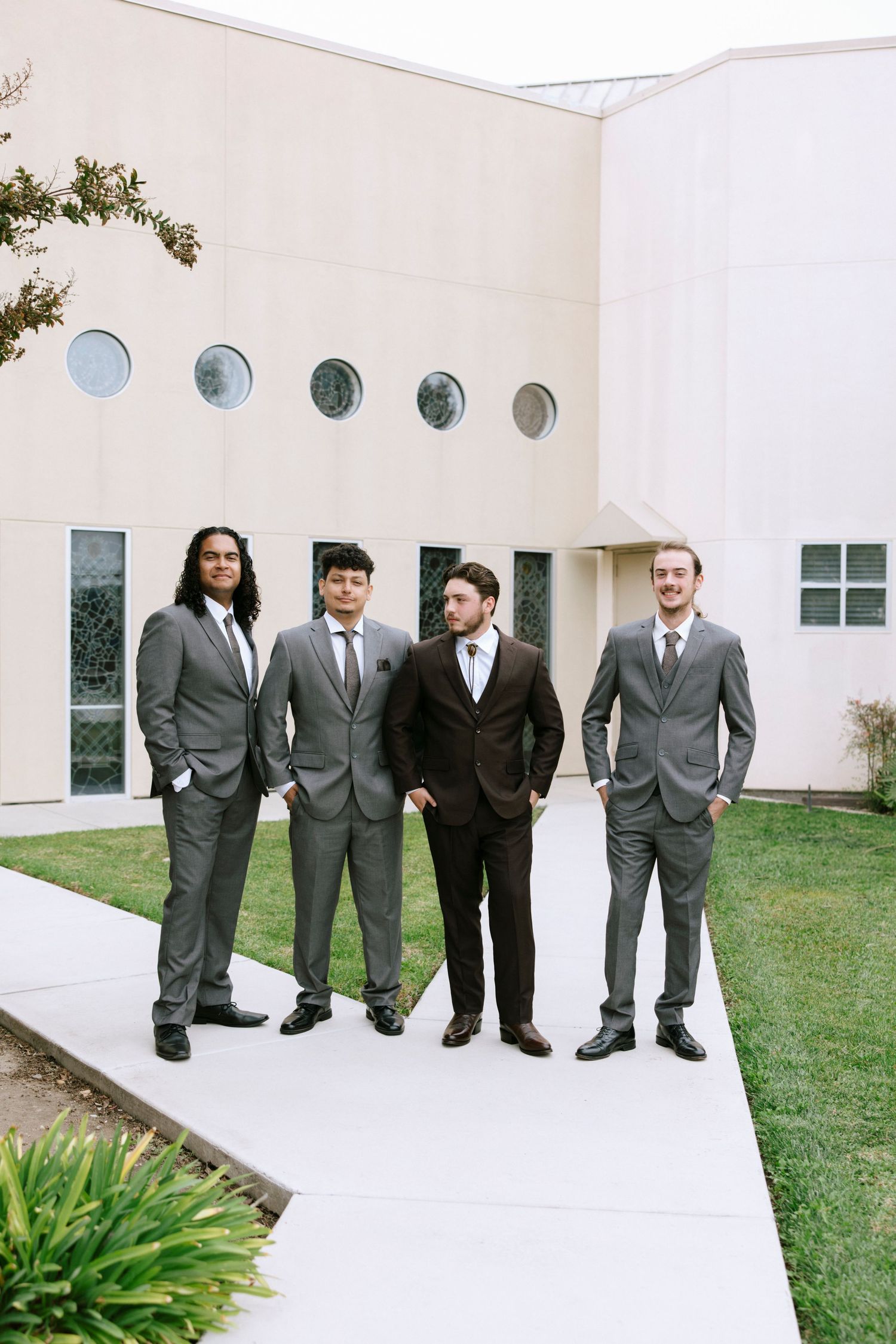 Four people in formal suits pose together on white walkway with modern building backdrop.