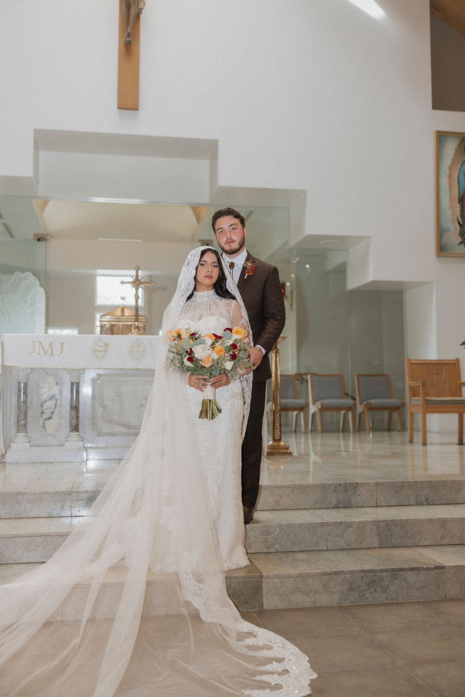 Wedding couple posing on church altar steps with flowing cathedral veil.