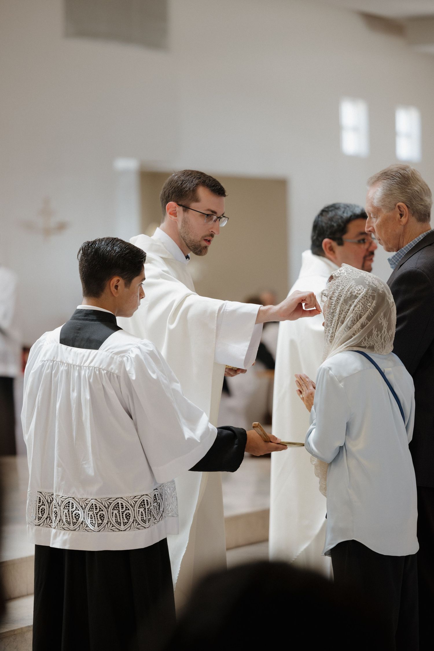 Clergy members in white robes and lace surplices distributing communion.
