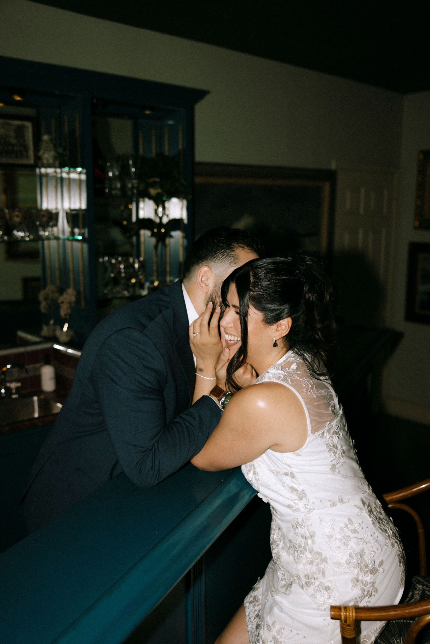 Couple shares an intimate moment at a bar reception venue with modern lighting fixtures.