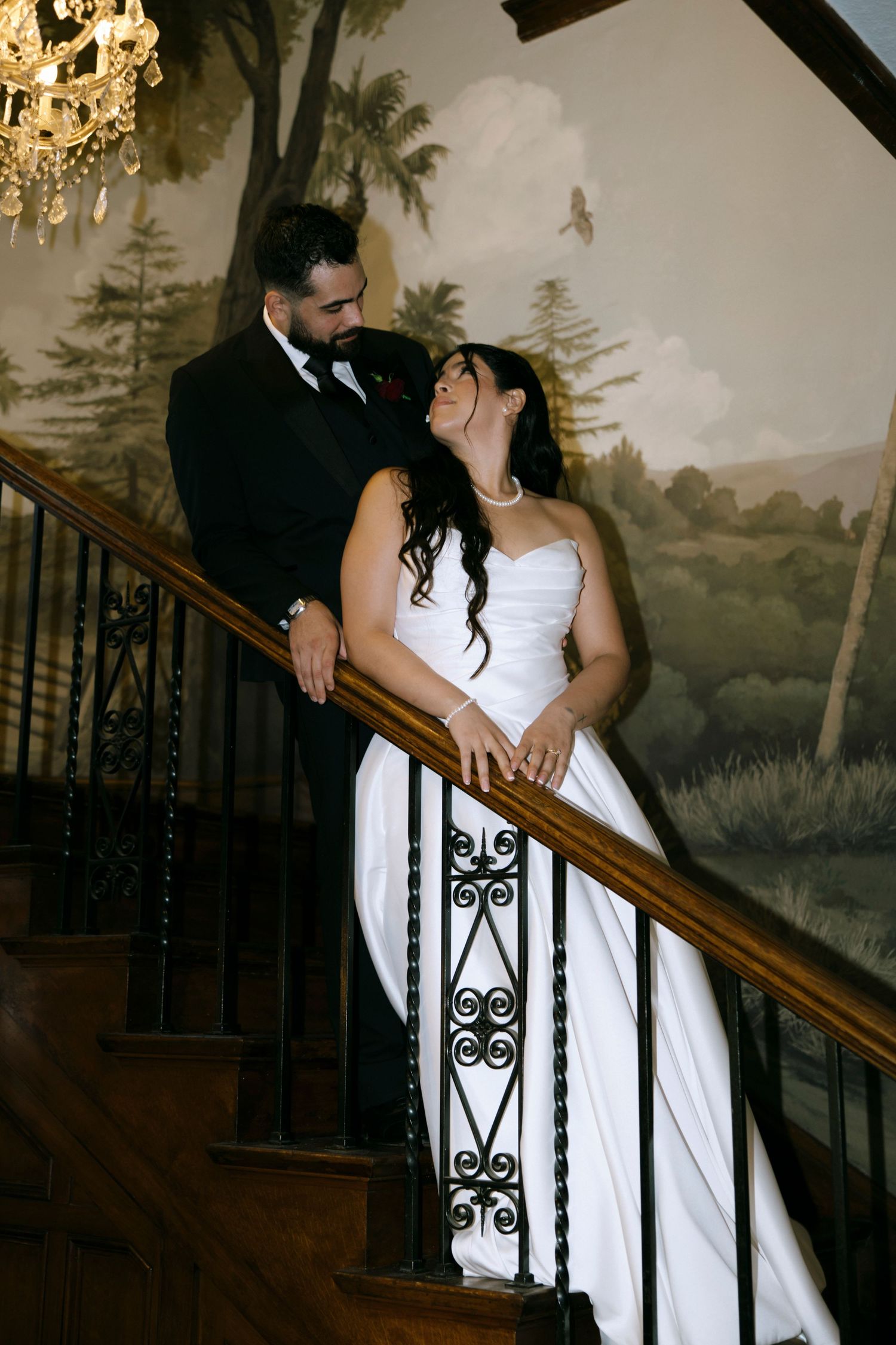 Romantic wedding couple posing on an elegant staircase with painted wall murals.