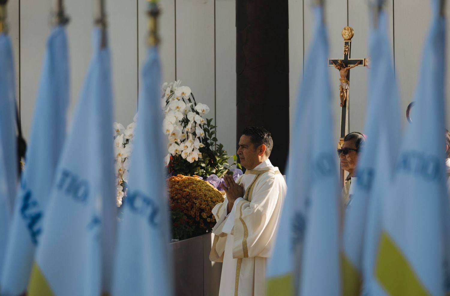 White-robed figures seated against a backdrop of blue banners during a religious ceremony.