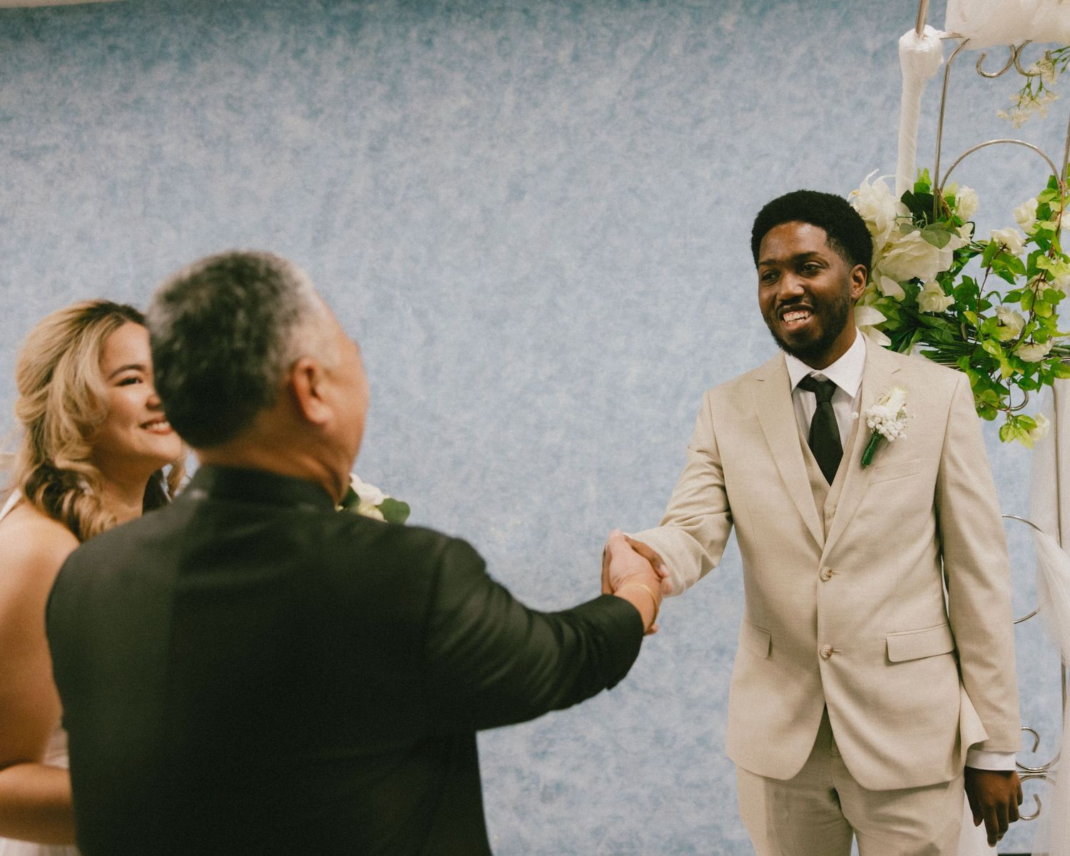 A celebratory handshake during a wedding ceremony under a floral arch.