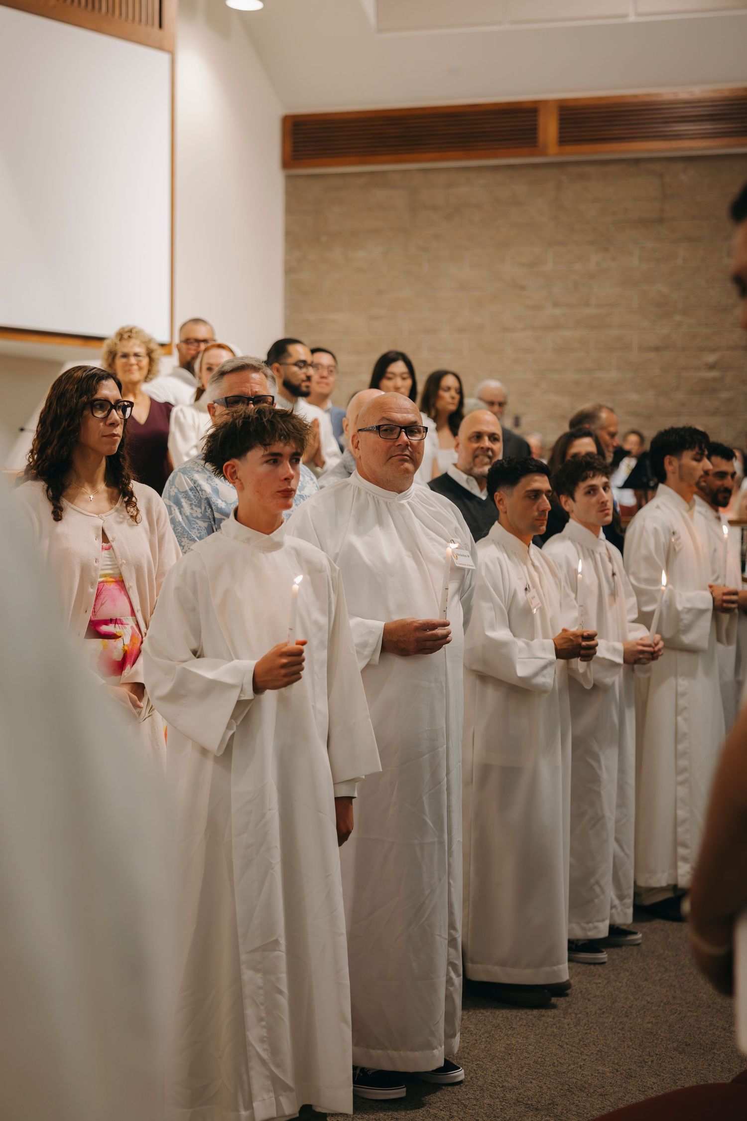 Group of newly baptized Catholics in white robes holding candles during Easter Vigil ceremony in church.