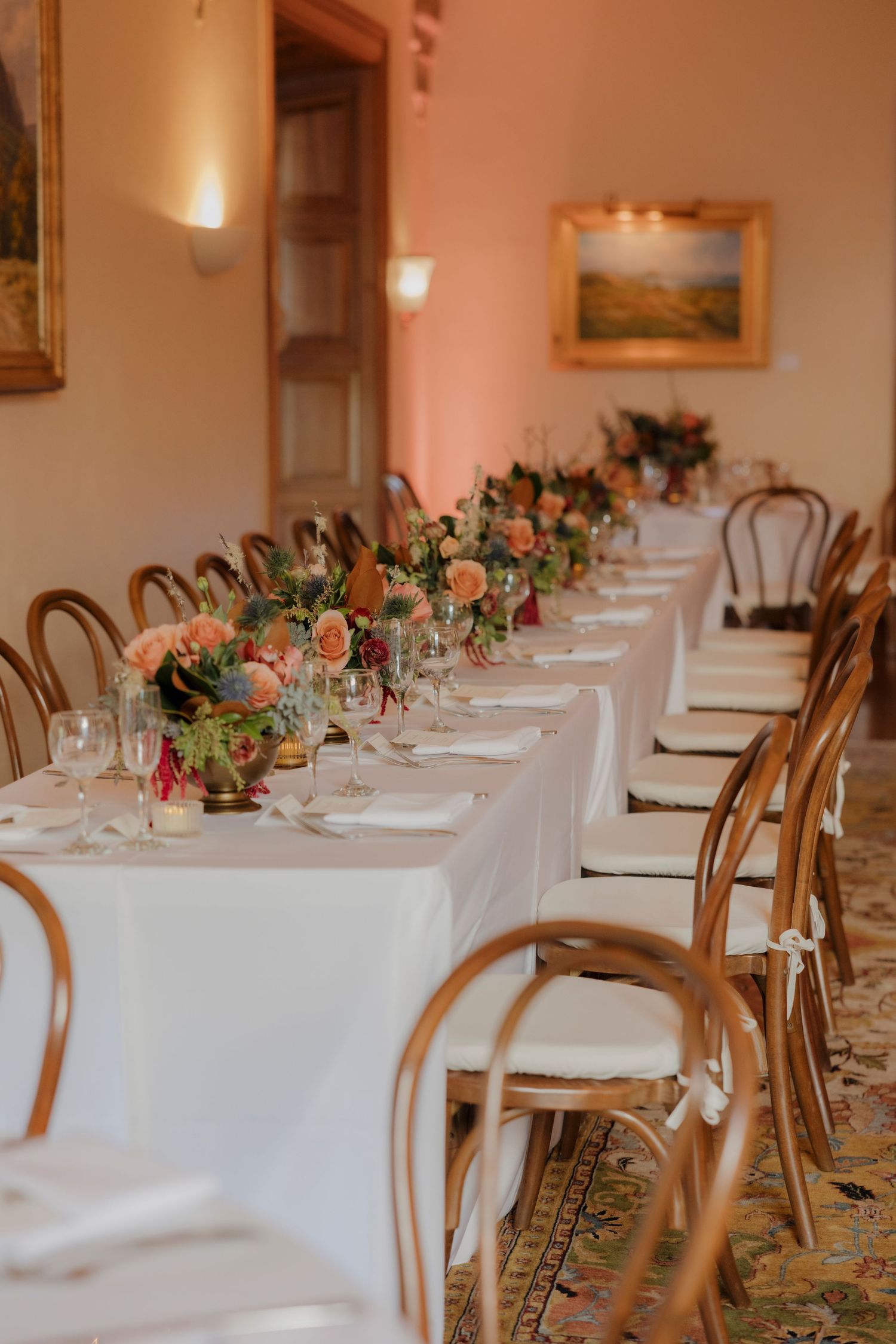 Wedding reception tables set with white linens, floral centerpieces and bentwood chairs.