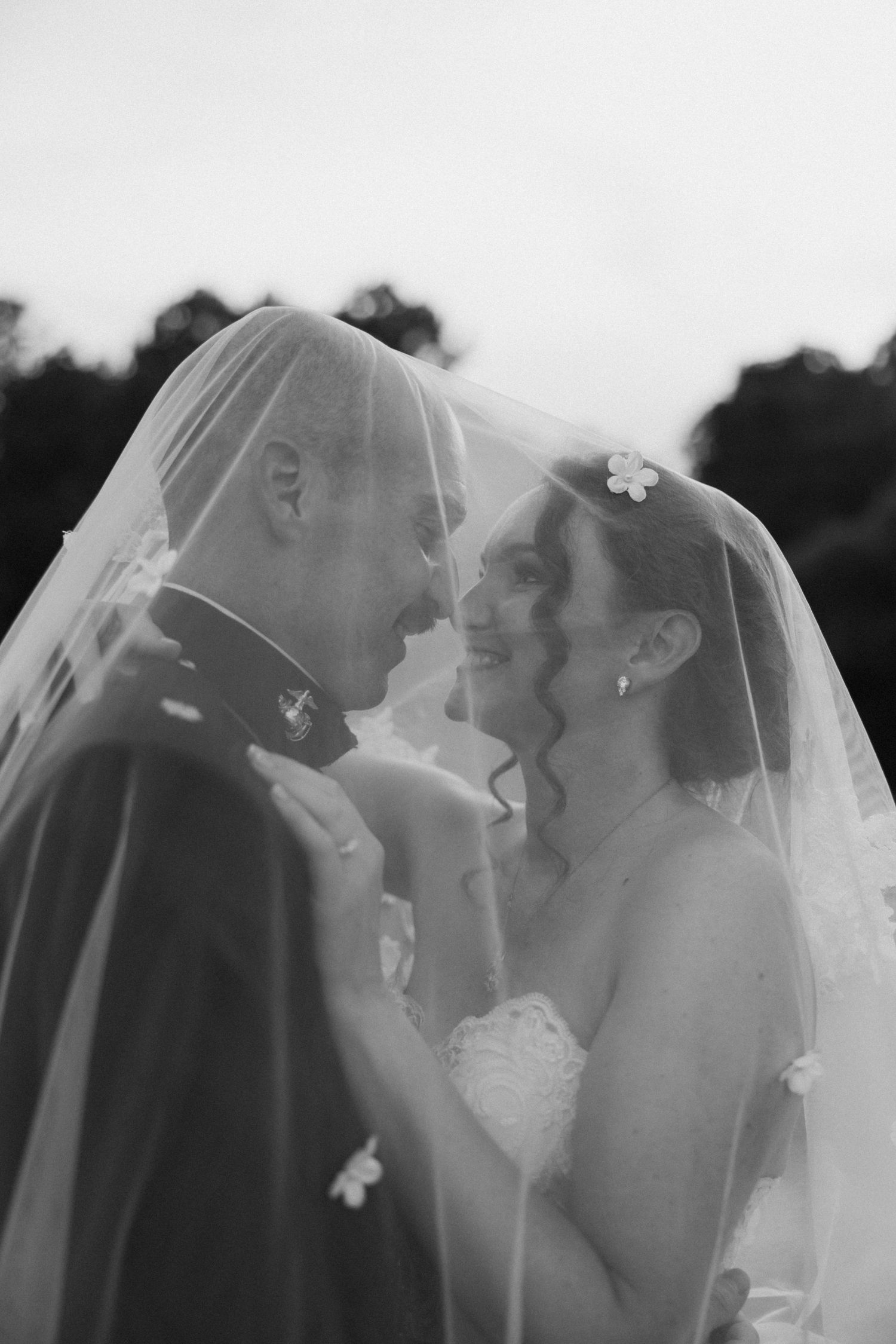 Black and white photo of a bride and groom sharing a romantic moment under her flowing veil on their wedding day.