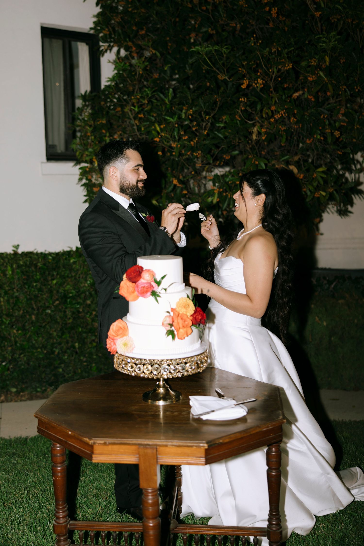 A couple shares a playful moment while cutting their wedding cake decorated with coral flowers.