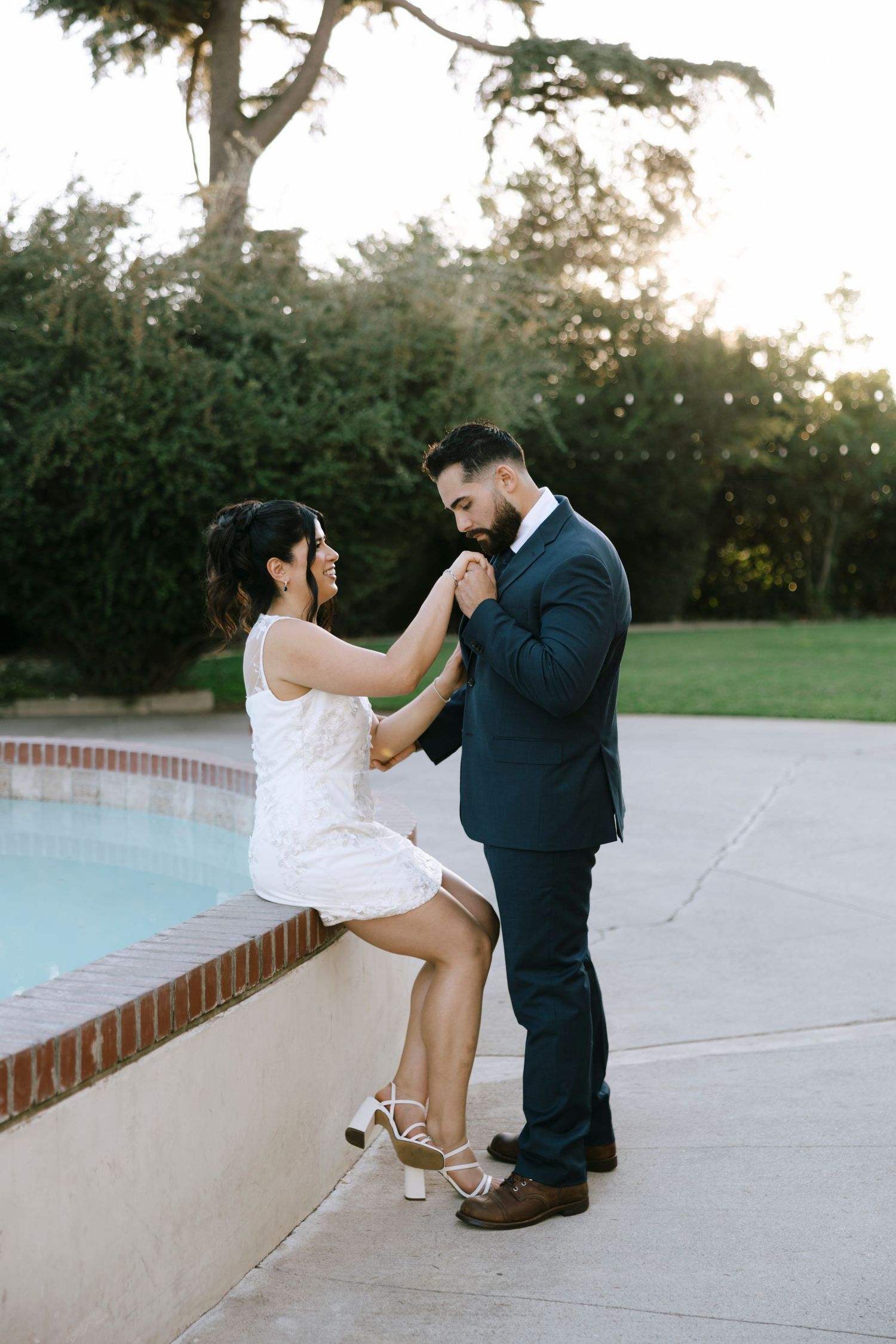 A couple sits together on a white ledge during an outdoor photoshoot.