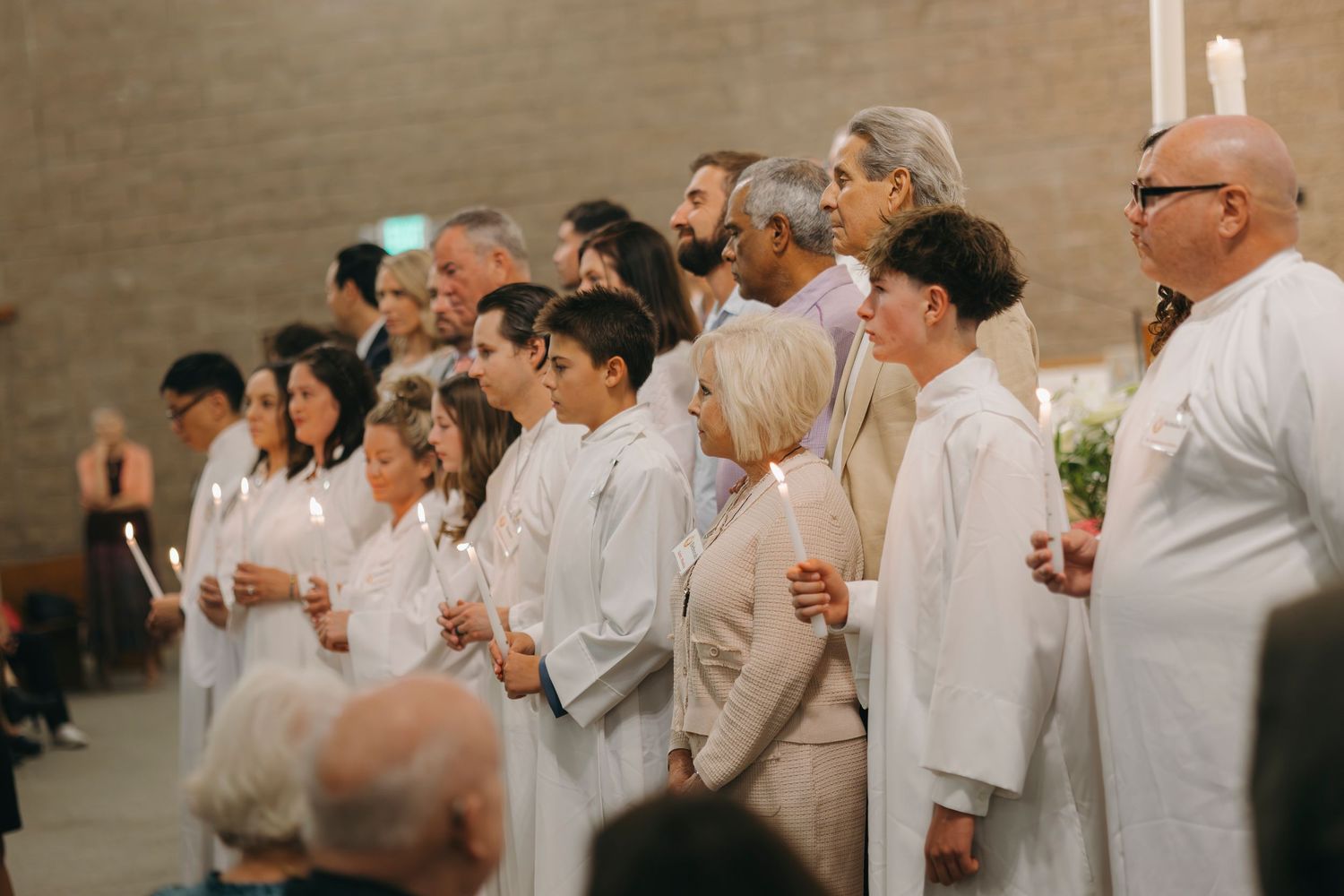 Group of white-robed catechumens holding candles during Easter Vigil initiation rites in a church.