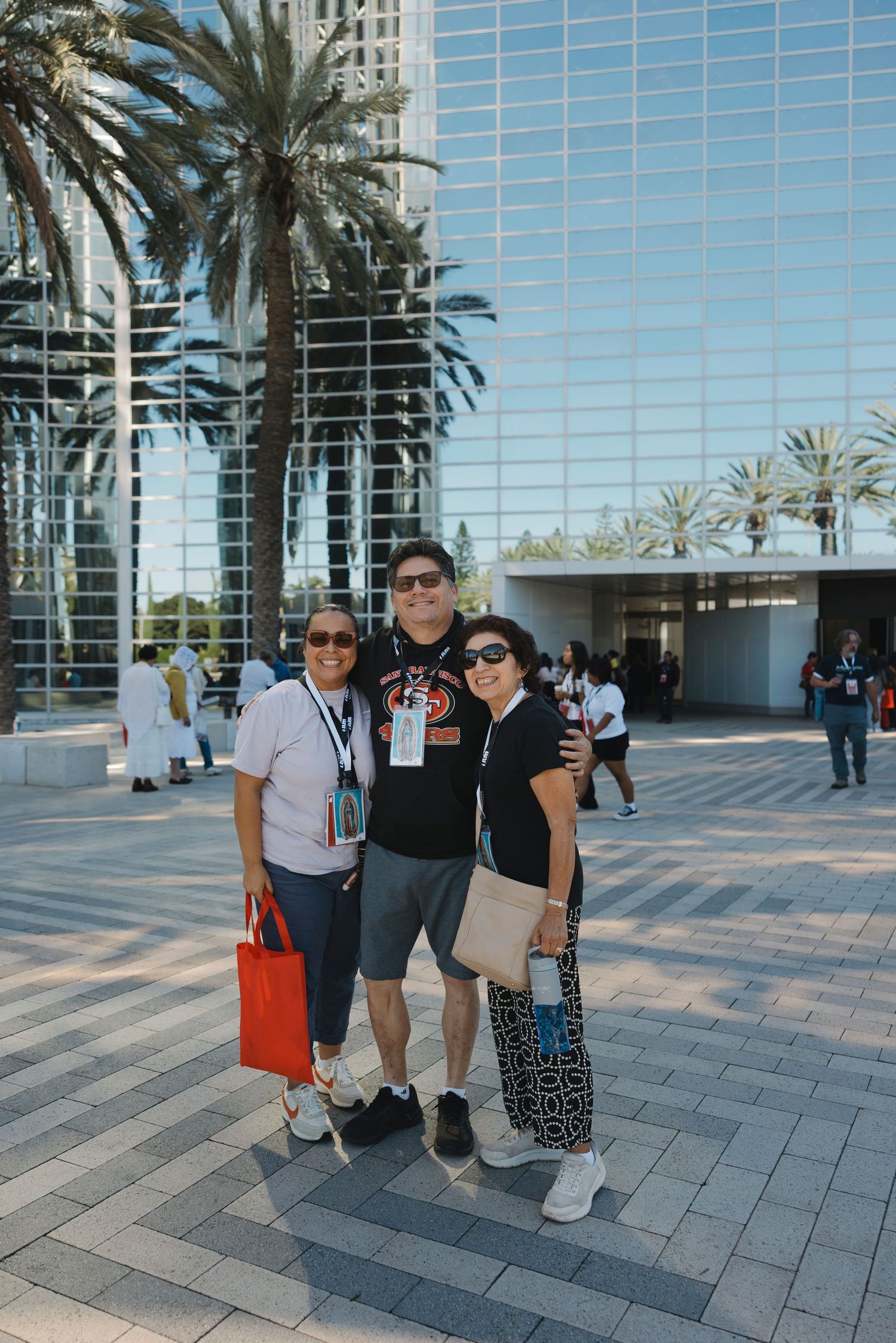 Three people standing together on a paved plaza with palm trees and glass buildings in the background.