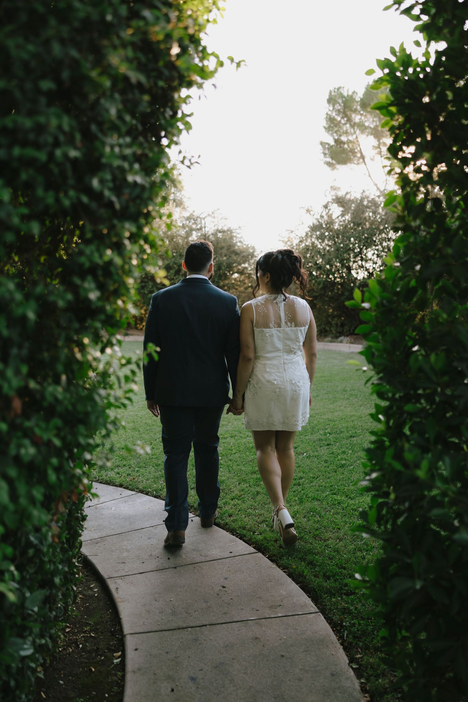 Couple walking together on concrete path surrounded by lush greenery.