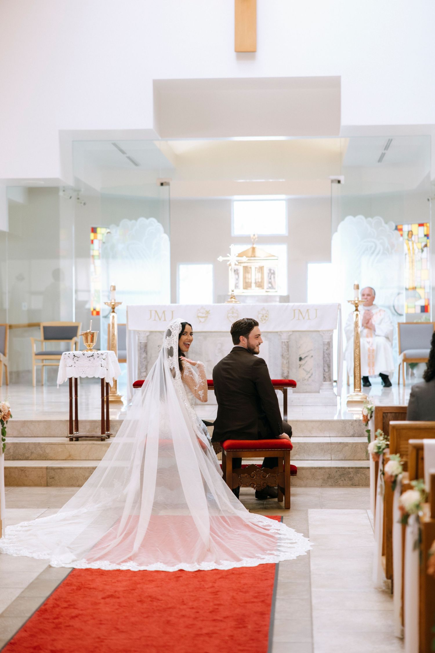 Wedding ceremony in modern church with red carpet aisle and flowing white veil.