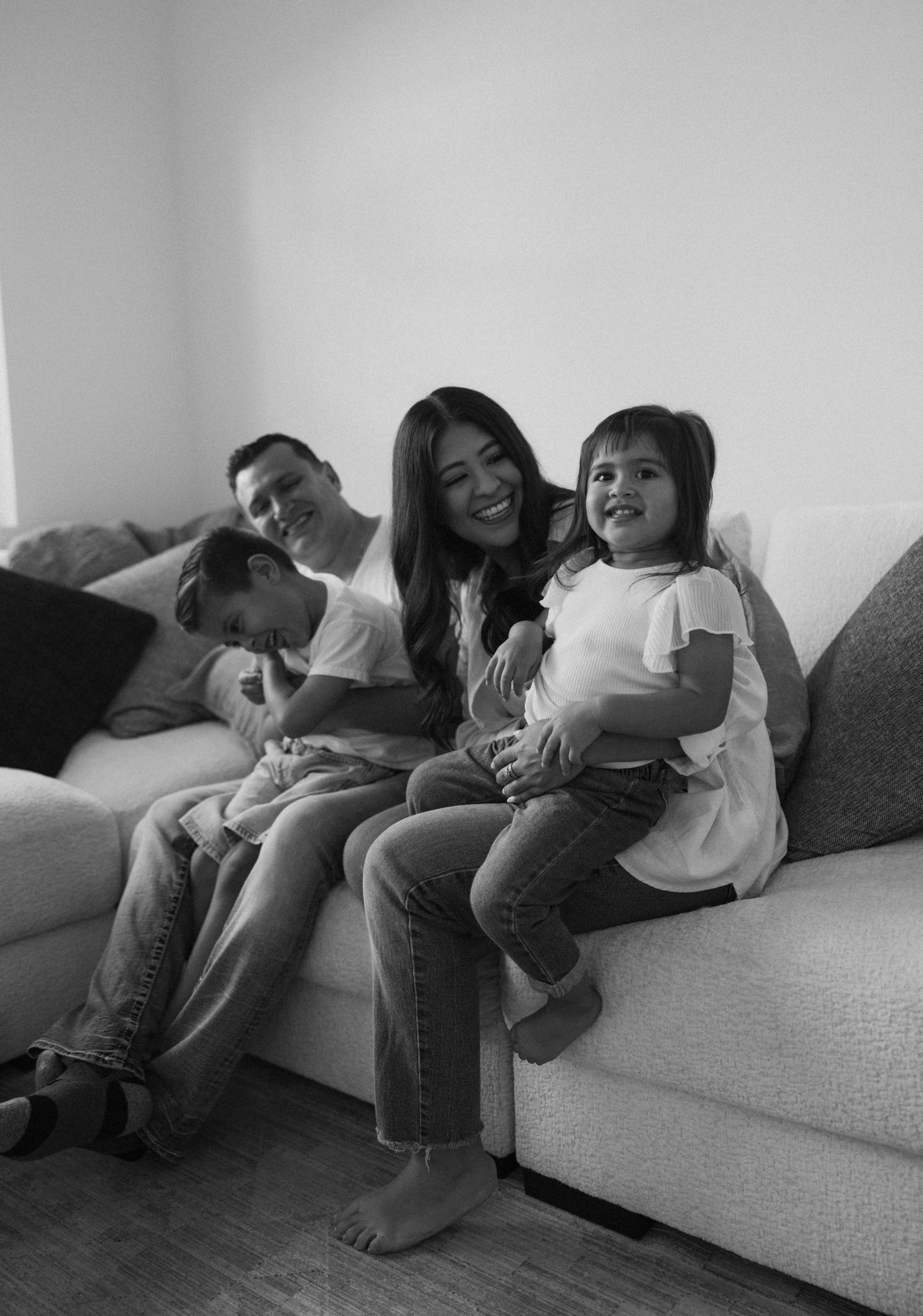 Family members lying together playfully on a gray couch in black and white.