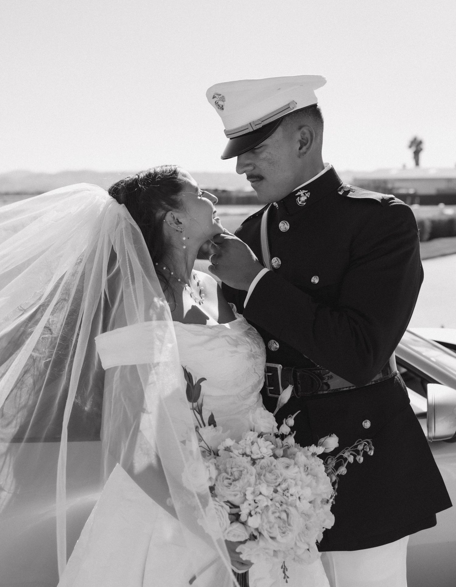 Black and white photo of military wedding couple sharing intimate moment with flowing veil.