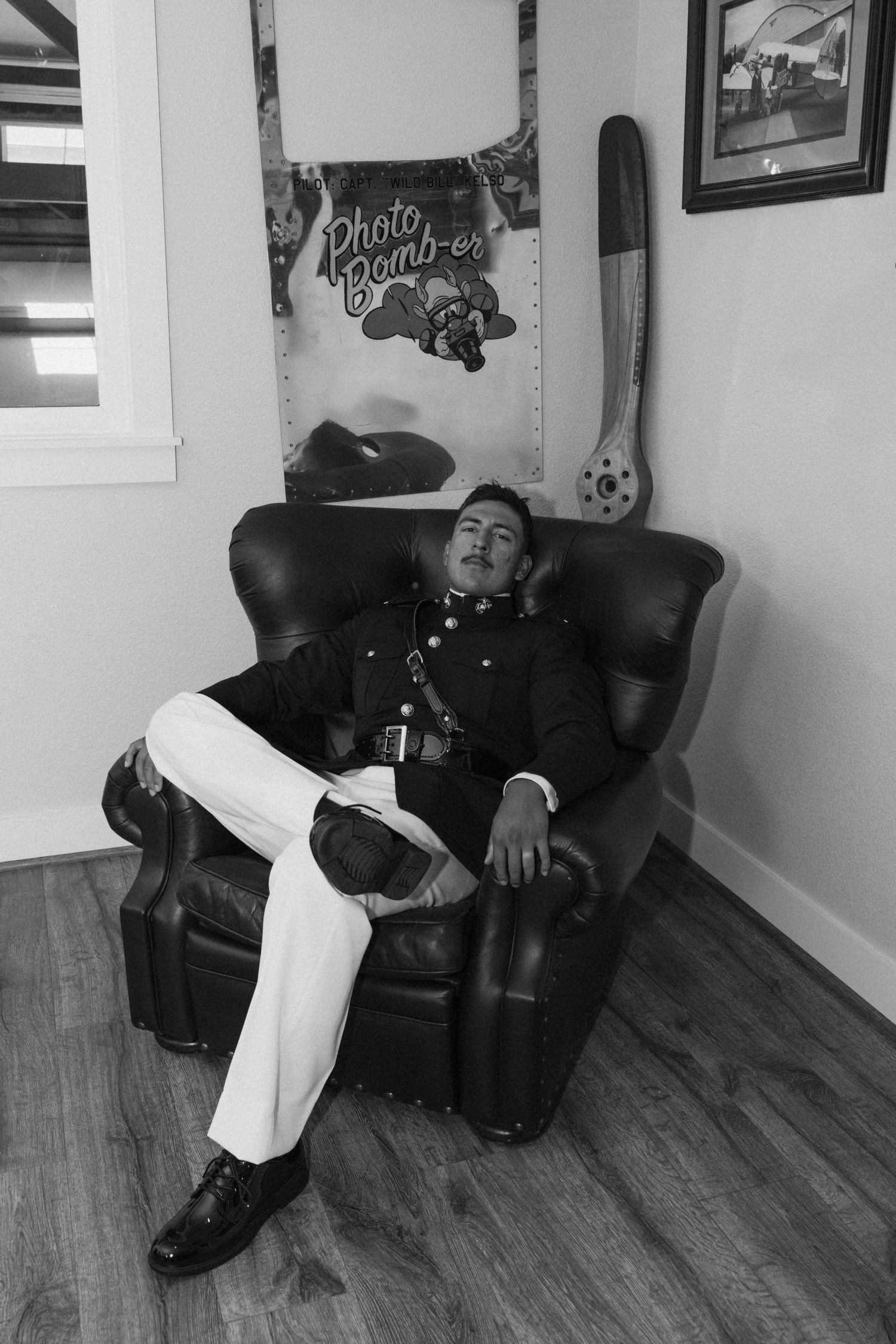 A person in formal attire reclines on a black leather couch in a room with framed wall art.