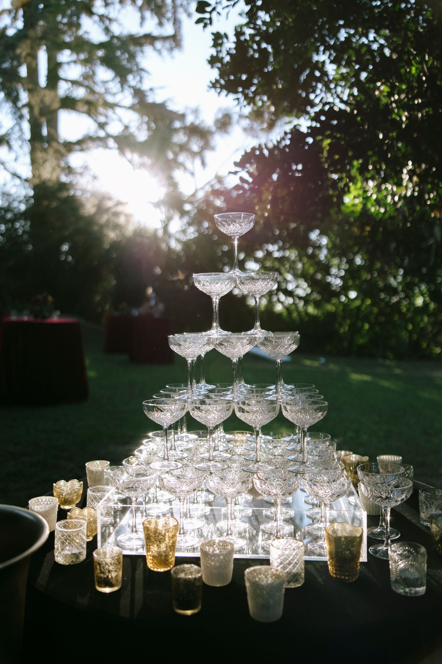 Elegant champagne tower with crystal glasses glowing in natural sunlight at an outdoor wedding.