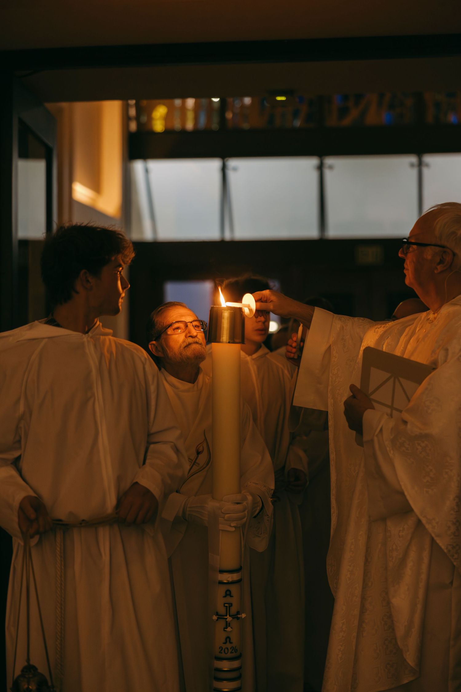 Priests in white robes lighting a large Paschal candle during a Catholic Easter Vigil ceremony.
