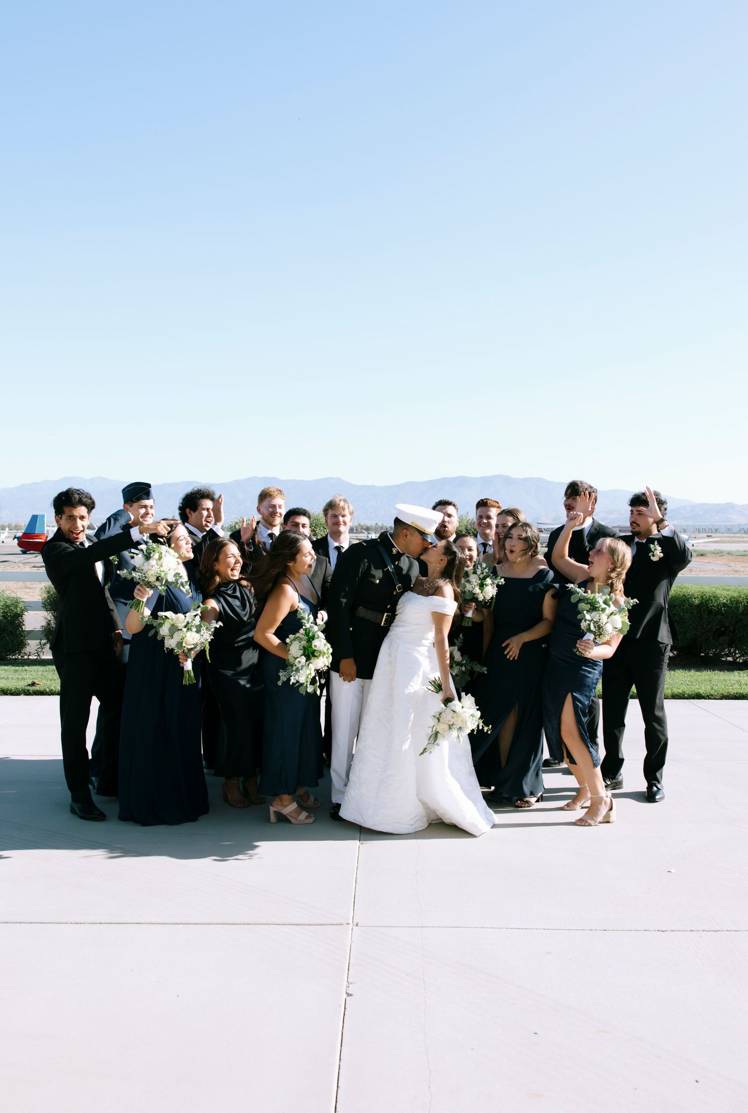 Wedding party poses casually outdoors with mountains in the background.