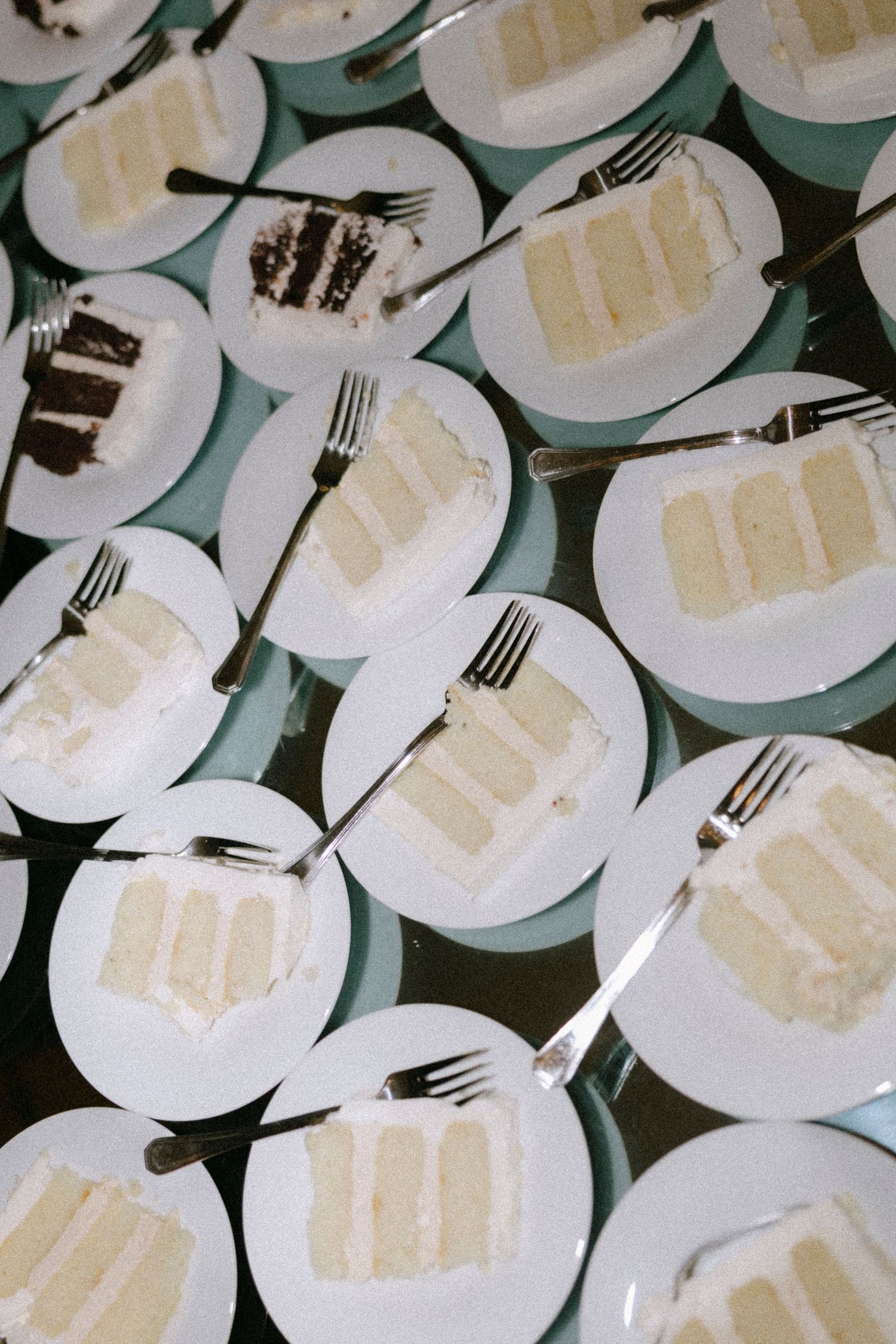 Multiple plates of white wedding cake slices arranged on turquoise plates with silver forks.