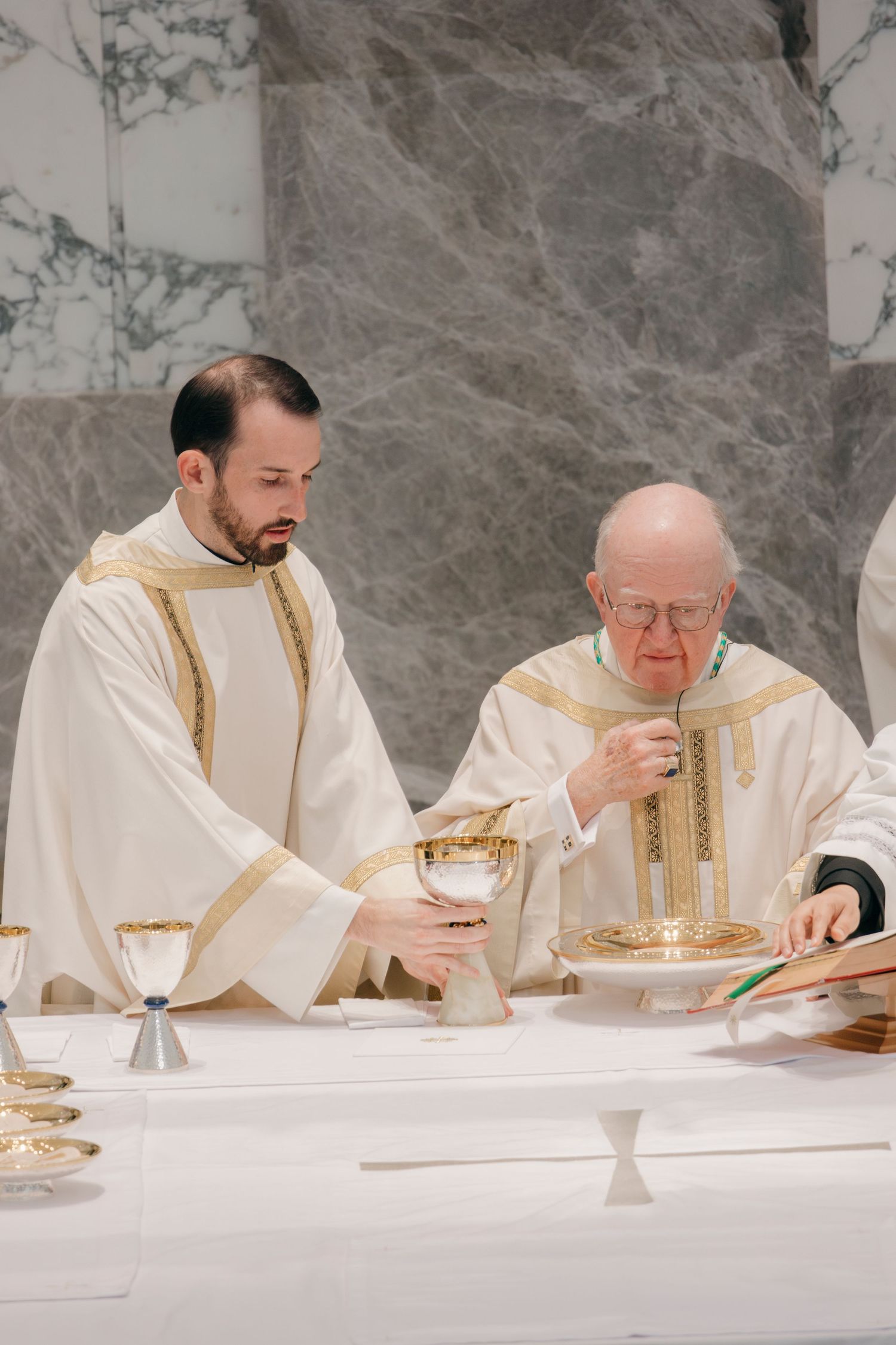 Clergy members in white vestments seated at marble altar during mass.