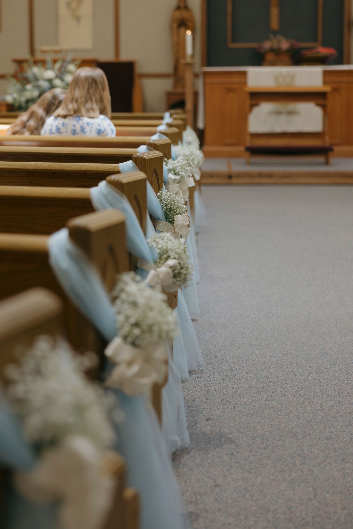 Church aisle decorated with baby's breath bouquets and white tulle on wooden pews for an elegant wedding ceremony.