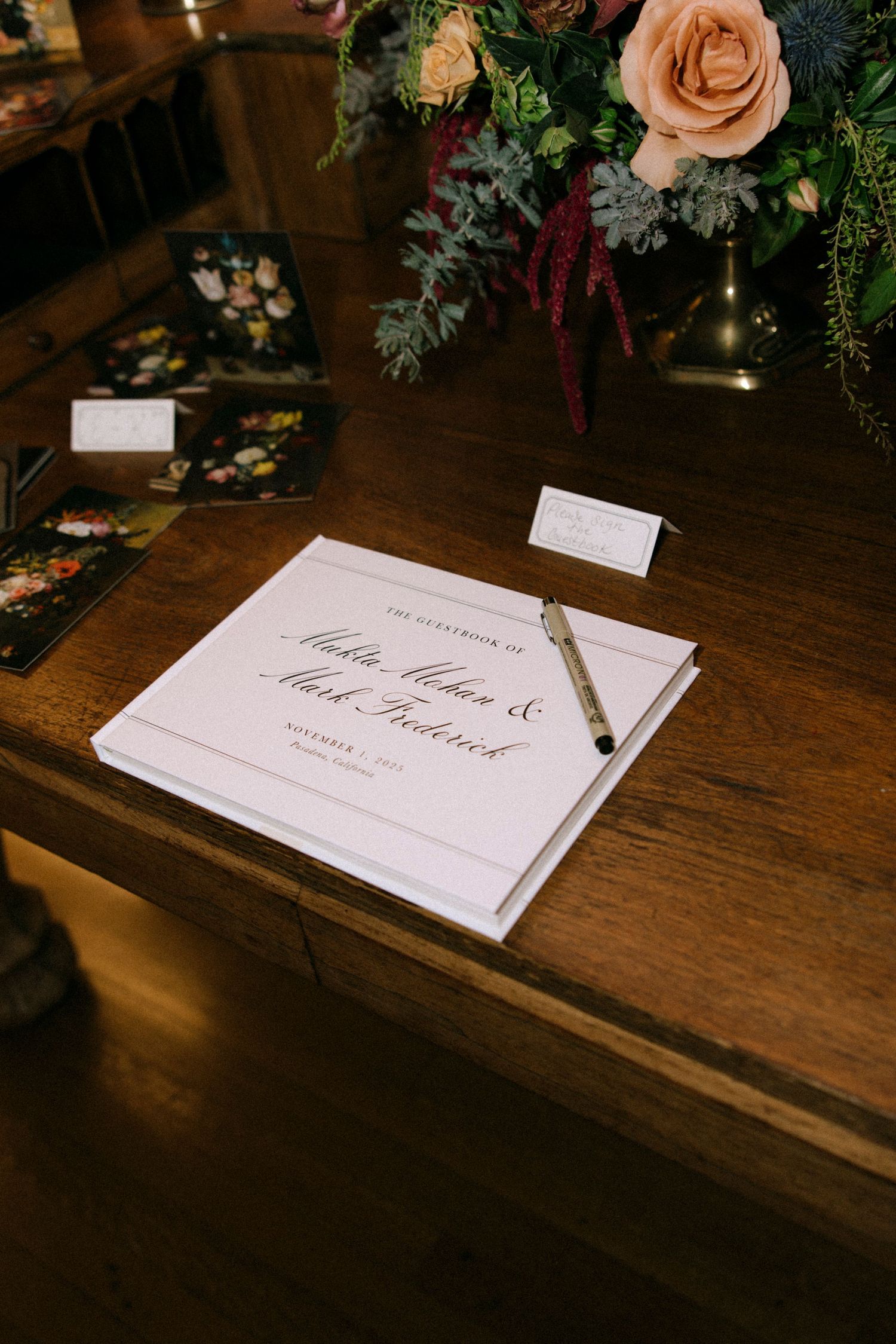 Wedding invitation cards displayed on wooden surface with peach roses and greenery decorations.