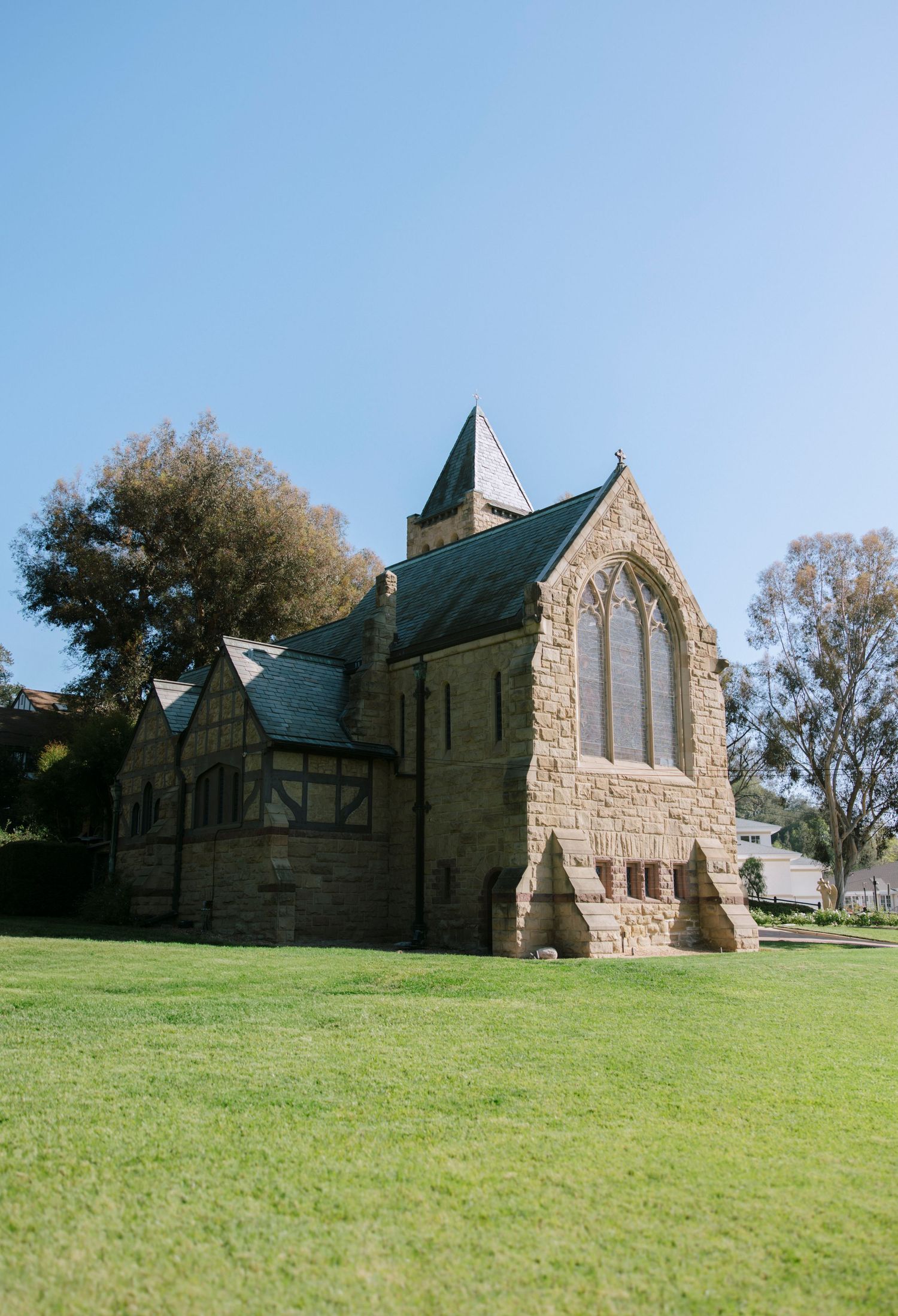 Historic stone church exterior with Gothic architecture sits on a grassy hillside in daylight.