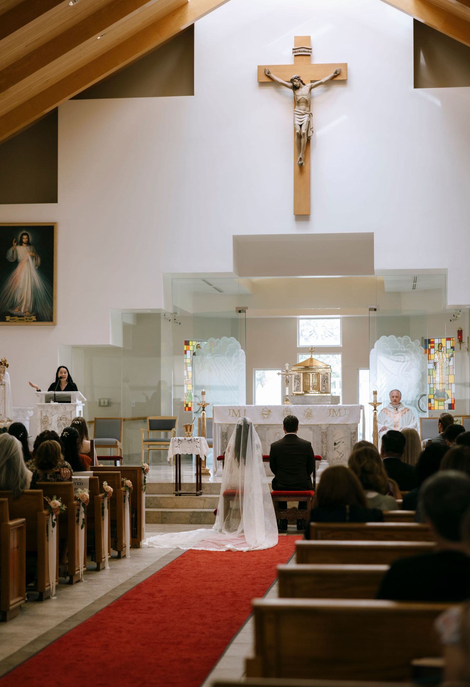 Wide angle view of a church wedding ceremony with a red carpet aisle and crucifix on the wall.