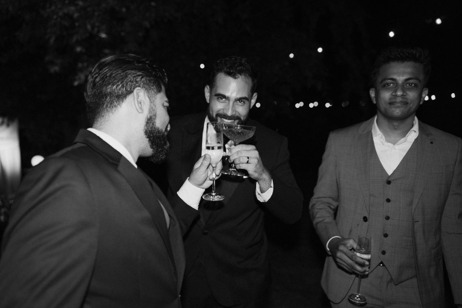 Three men in formal attire toasting drinks at a nighttime event.
