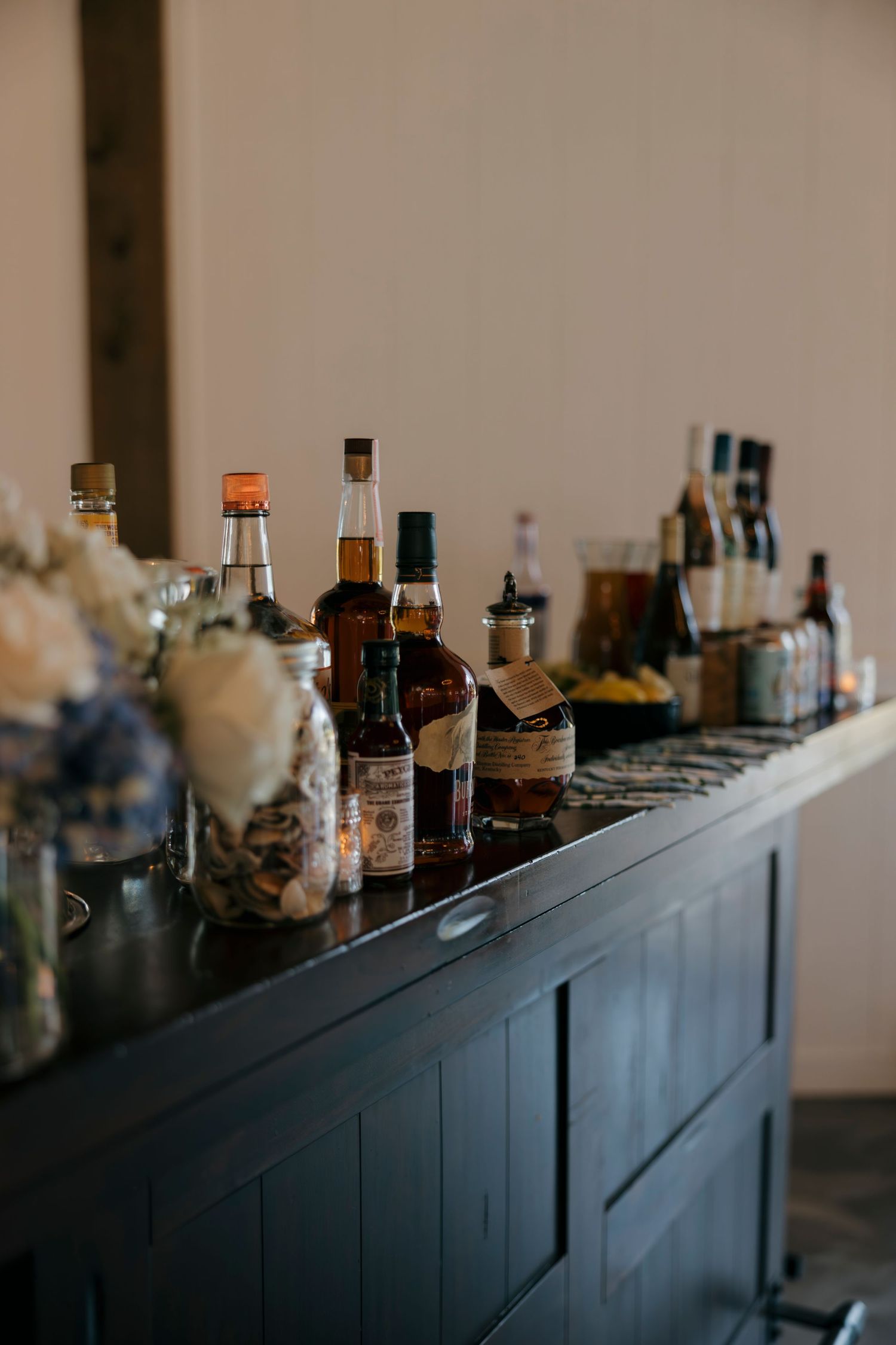 A dark wooden bar counter lined with whiskey bottles and floral arrangements at an elegant event venue.