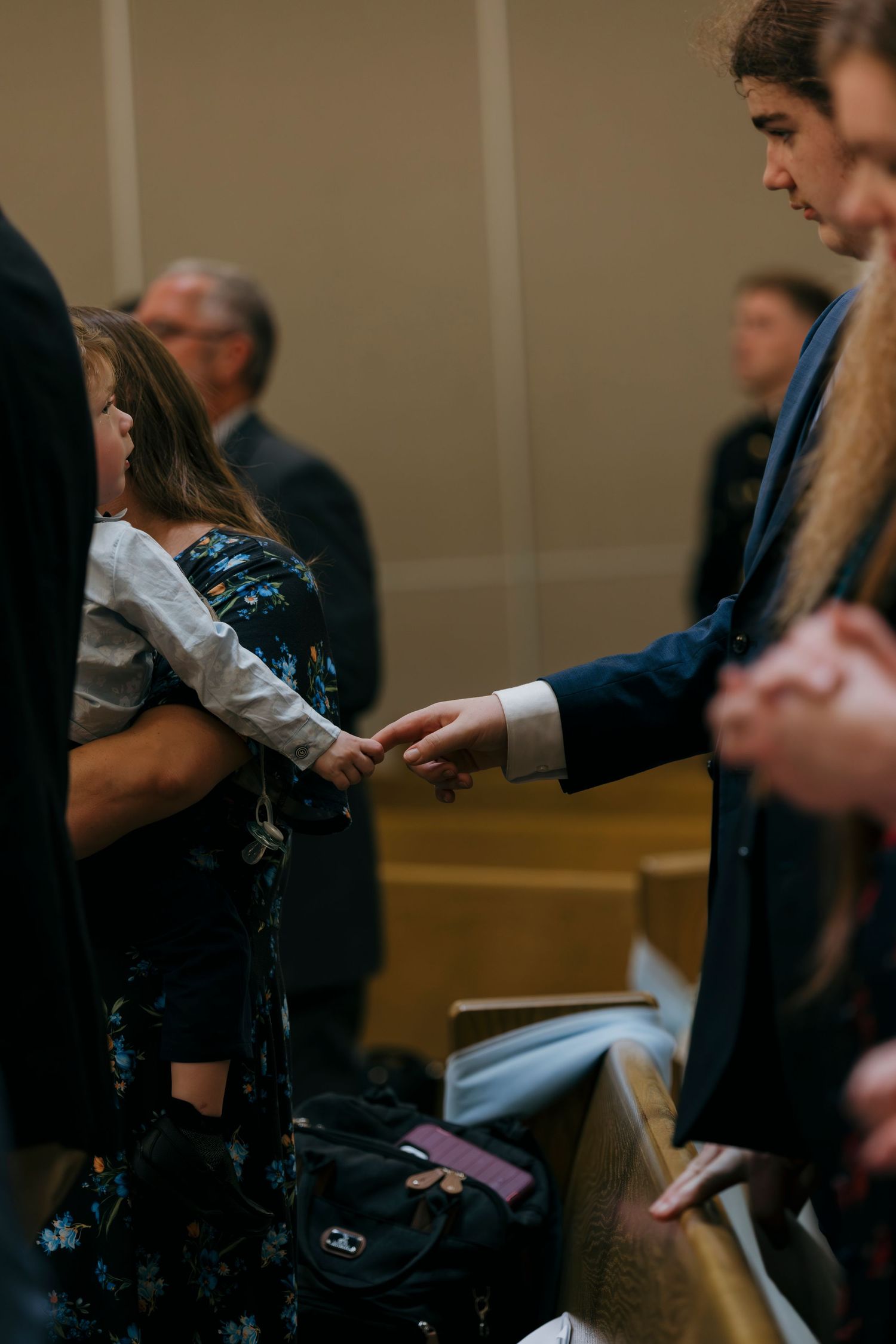 Man in blue suit holding hands with a young girl in a floral dress during a church gathering ceremony.