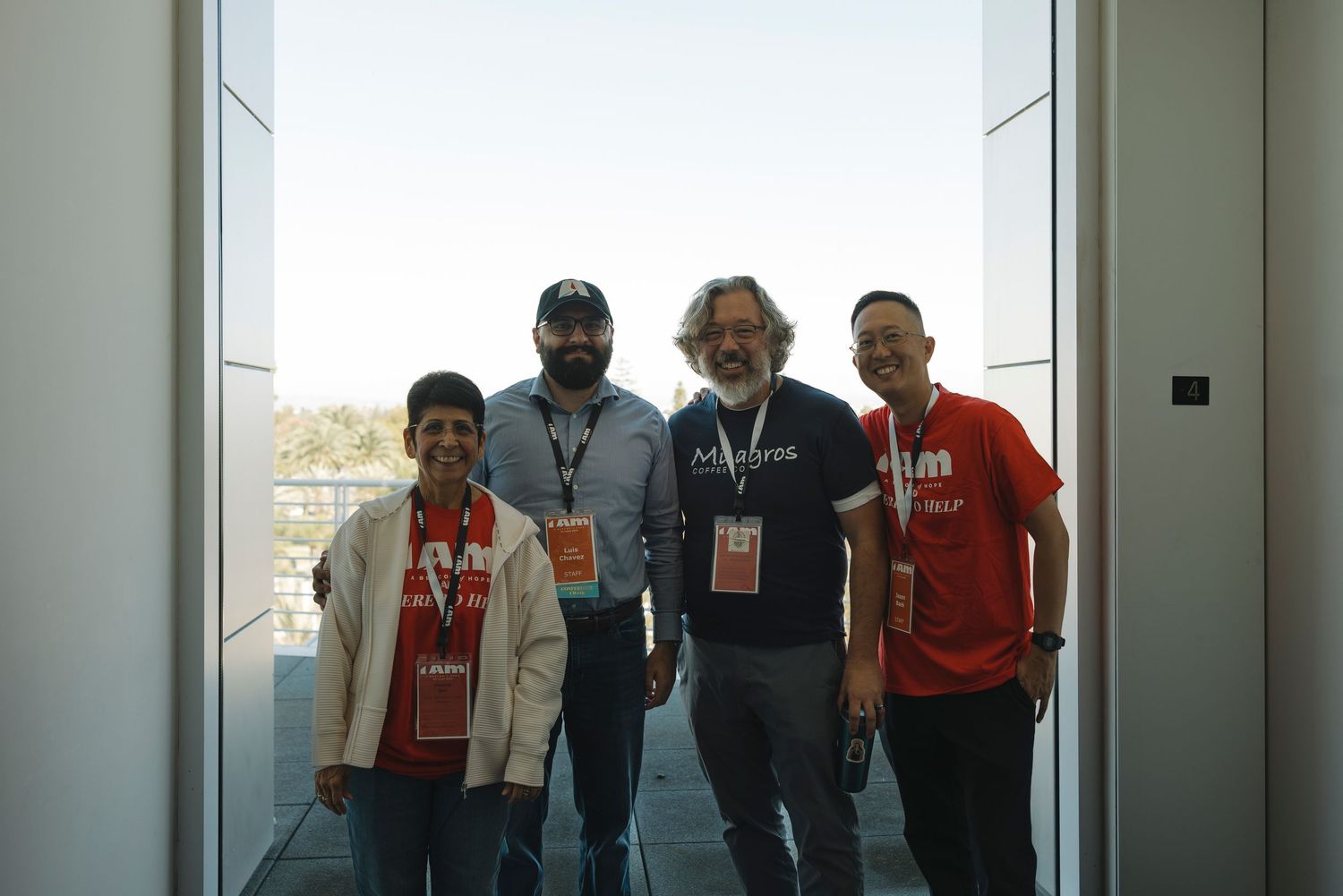 A group of people stand together in a bright hallway against a window backdrop.