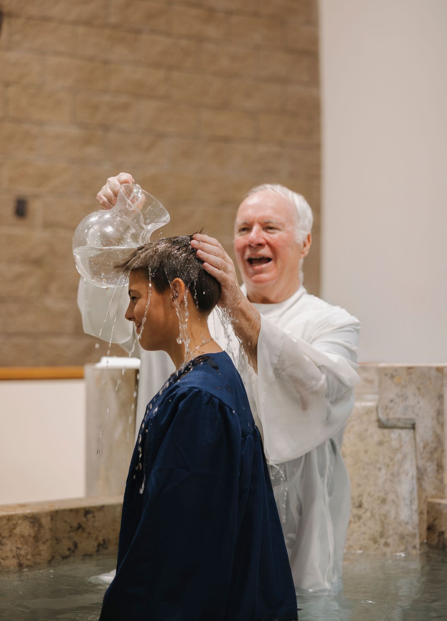 Joyful priest pours water over womans head during full immersion baptism at Easter Vigil.