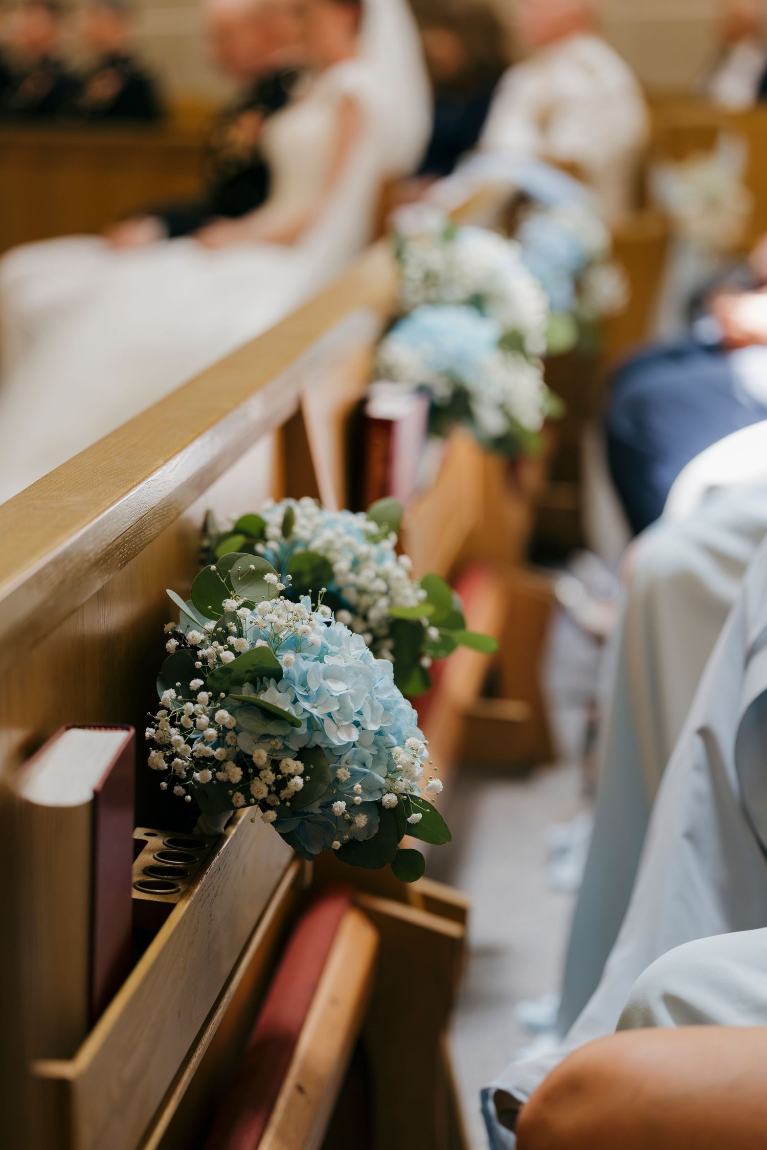 Blue hydrangea and baby's breath bouquets decorating wooden church pews at an elegant wedding ceremony.