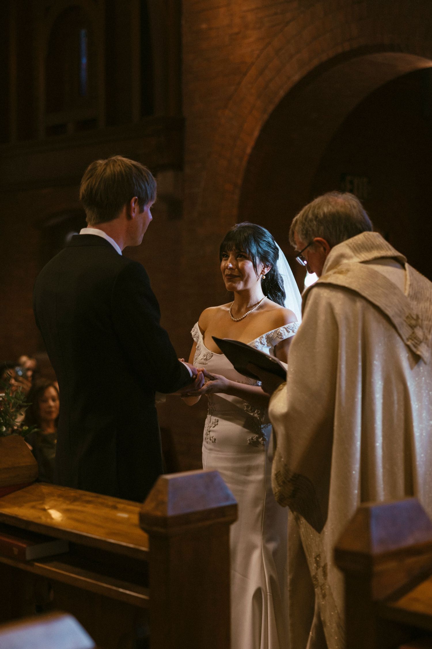 Wedding ceremony participants in white and black attire at church altar.