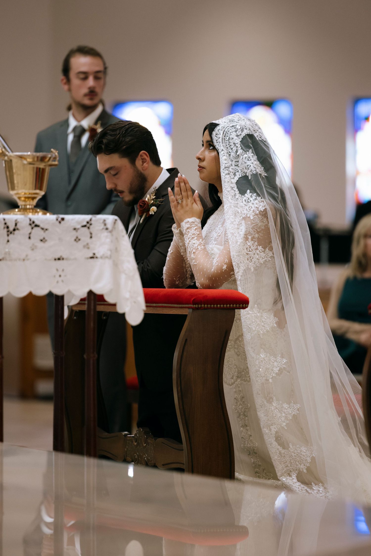 Wedding ceremony in progress showing bride's lace veil and church pews.