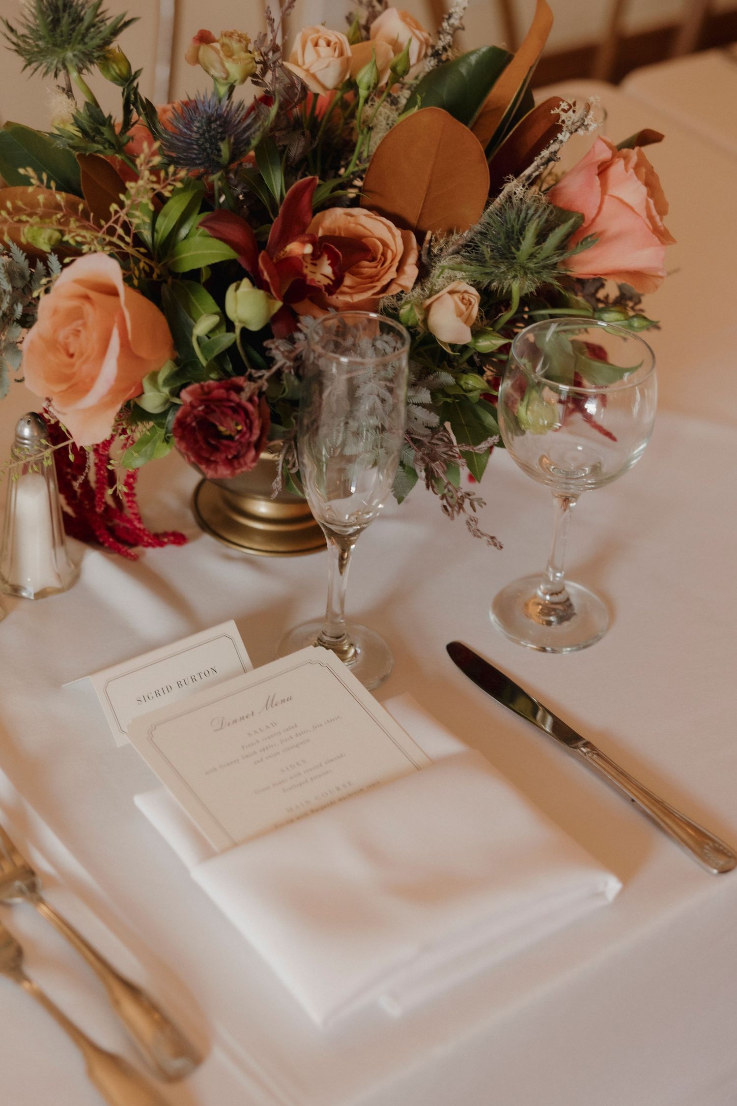 Elegant place setting with menu card and floral centerpiece on white tablecloth.