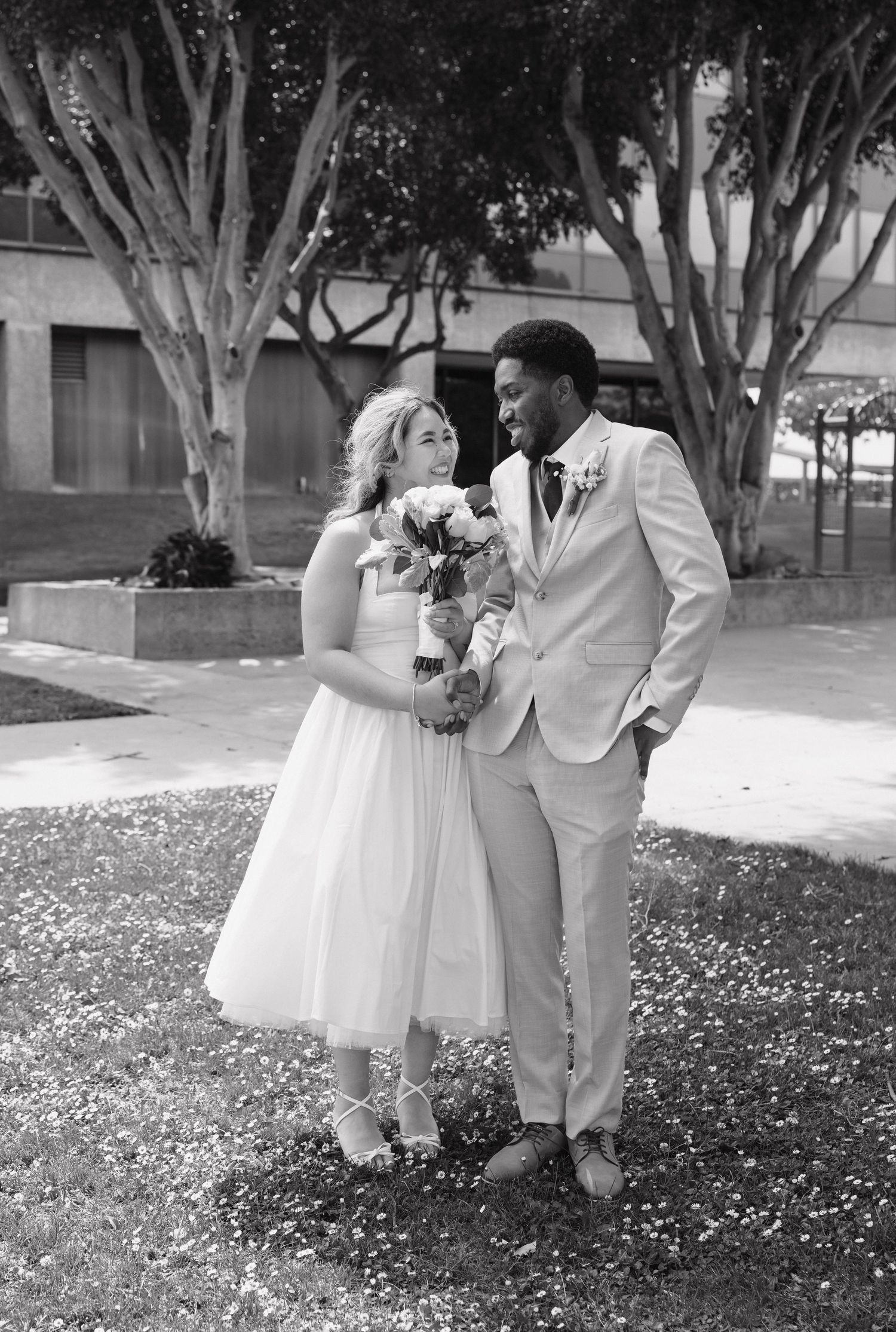 Elegant black and white portrait of newlyweds posing outdoors among trees.