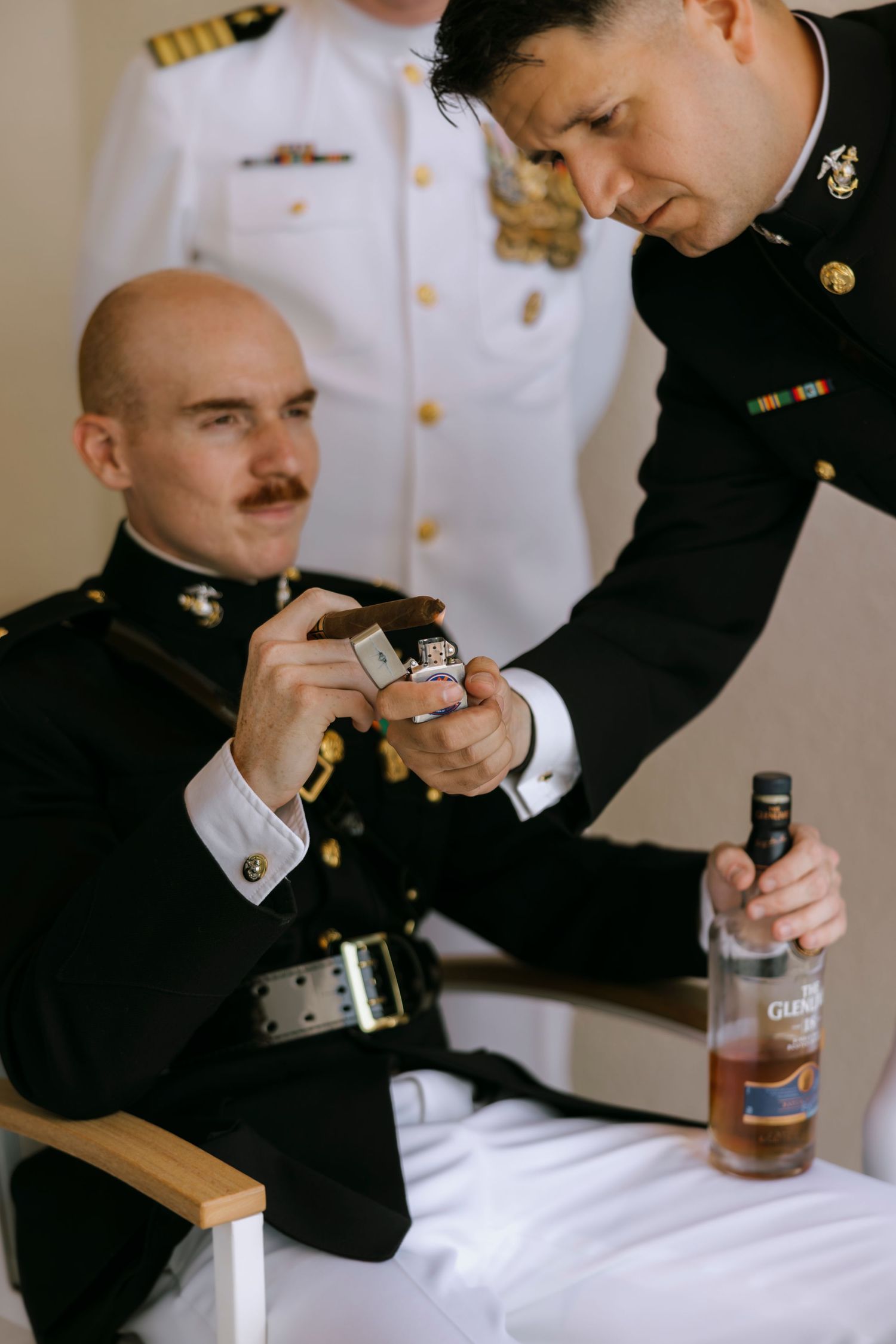 Two military officers in dress uniforms lighting a cigar, with a bottle of Glenfiddich whisky nearby.