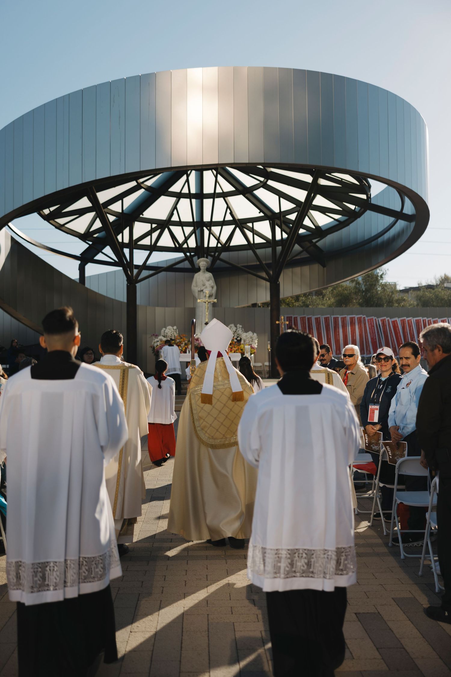 Religious ceremony under a modern circular canopy with clergy in white vestments.