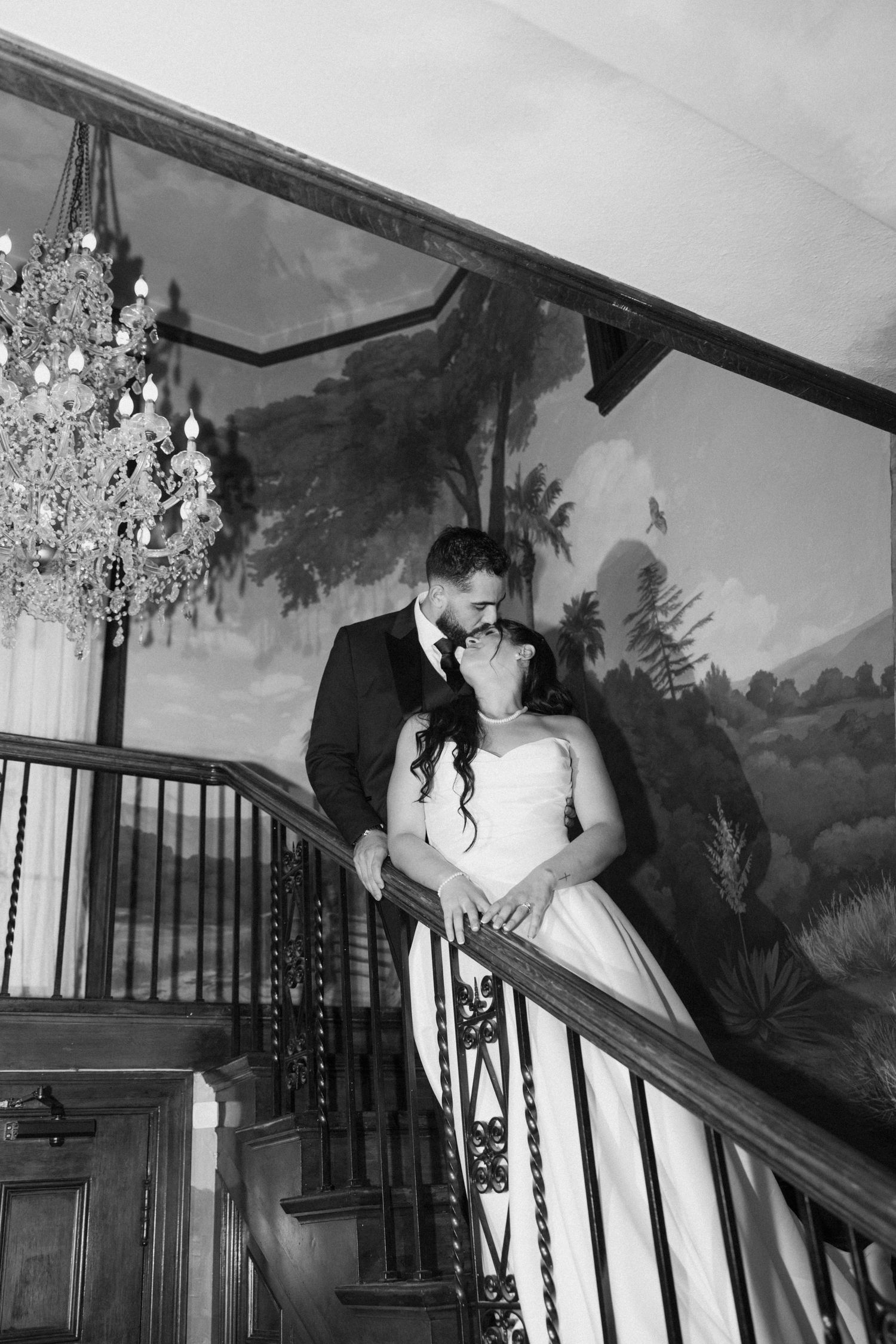 Dramatic black and white photo of couple on staircase with vintage wall mural backdrop.