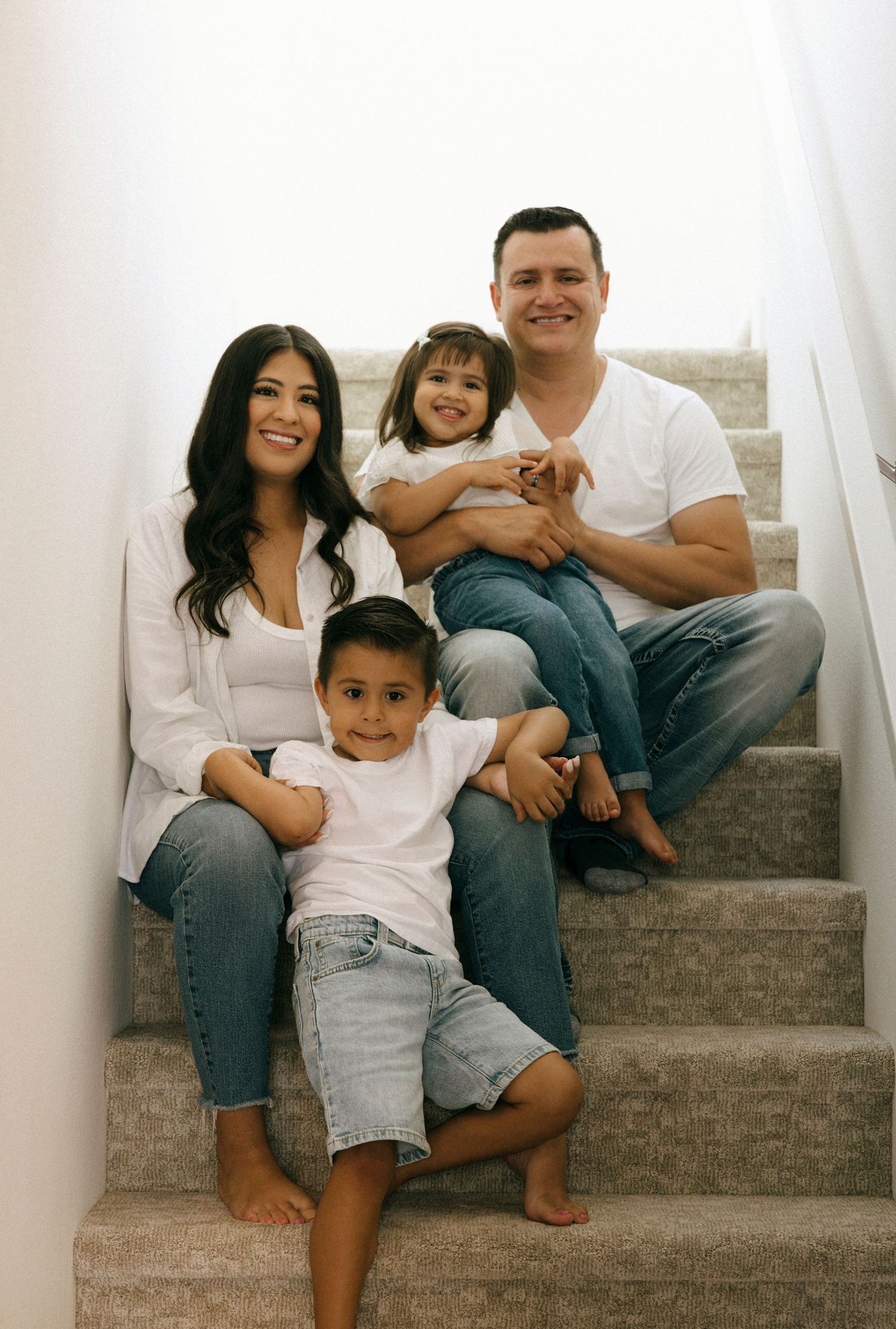 Happy family sitting together on carpeted stairs in casual attire.