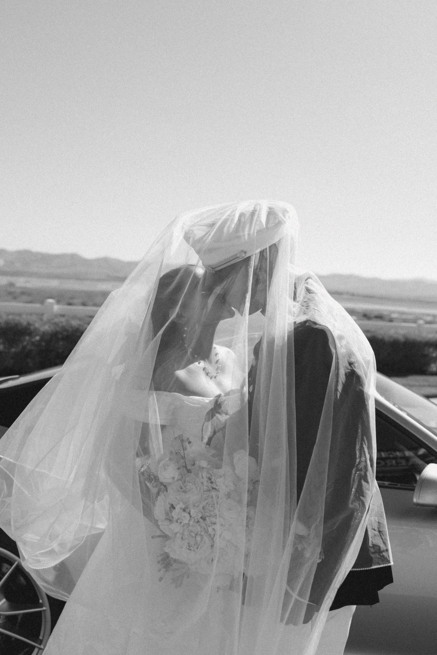 Black and white portrait of a couple sharing a tender moment under a wedding veil.