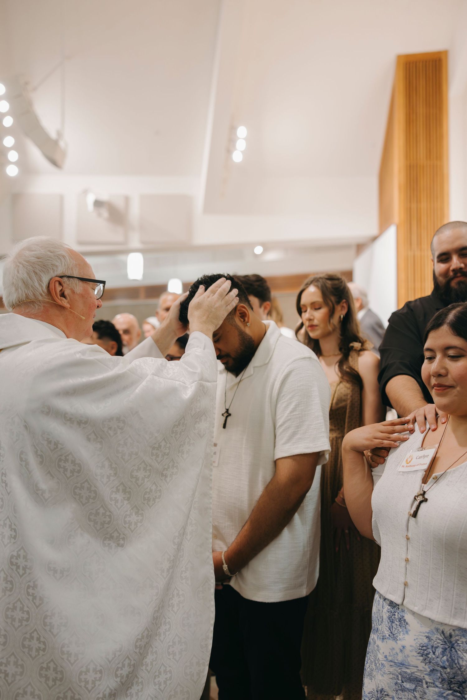 Catholic priest anointing young man with chrism oil during Confirmation sacrament ceremony.